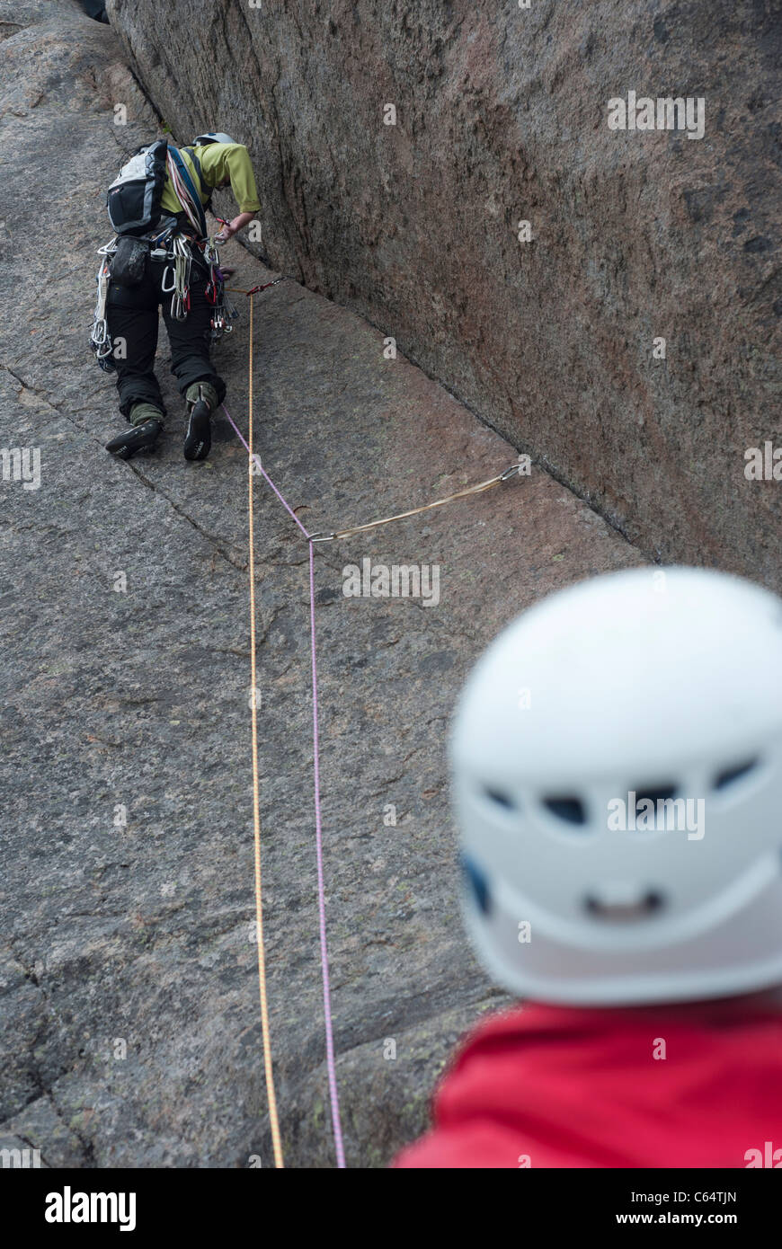 A male climber belaying a female climber as she climbs up a granite