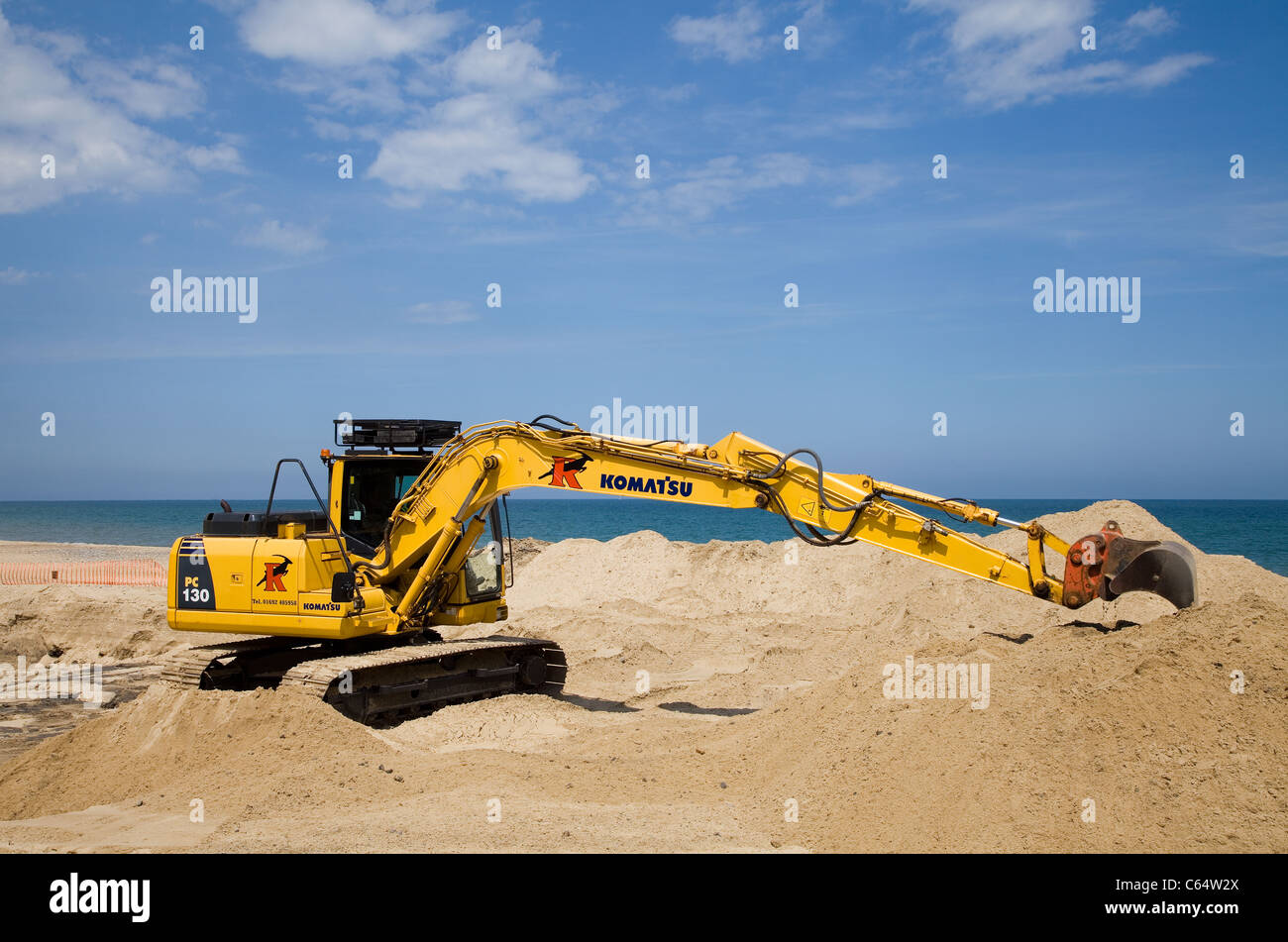 Komatsu PC130 seen here on a beach digging a trench for an archaeological dig Blue sea & sky with fluff white clouds Stock Photo
