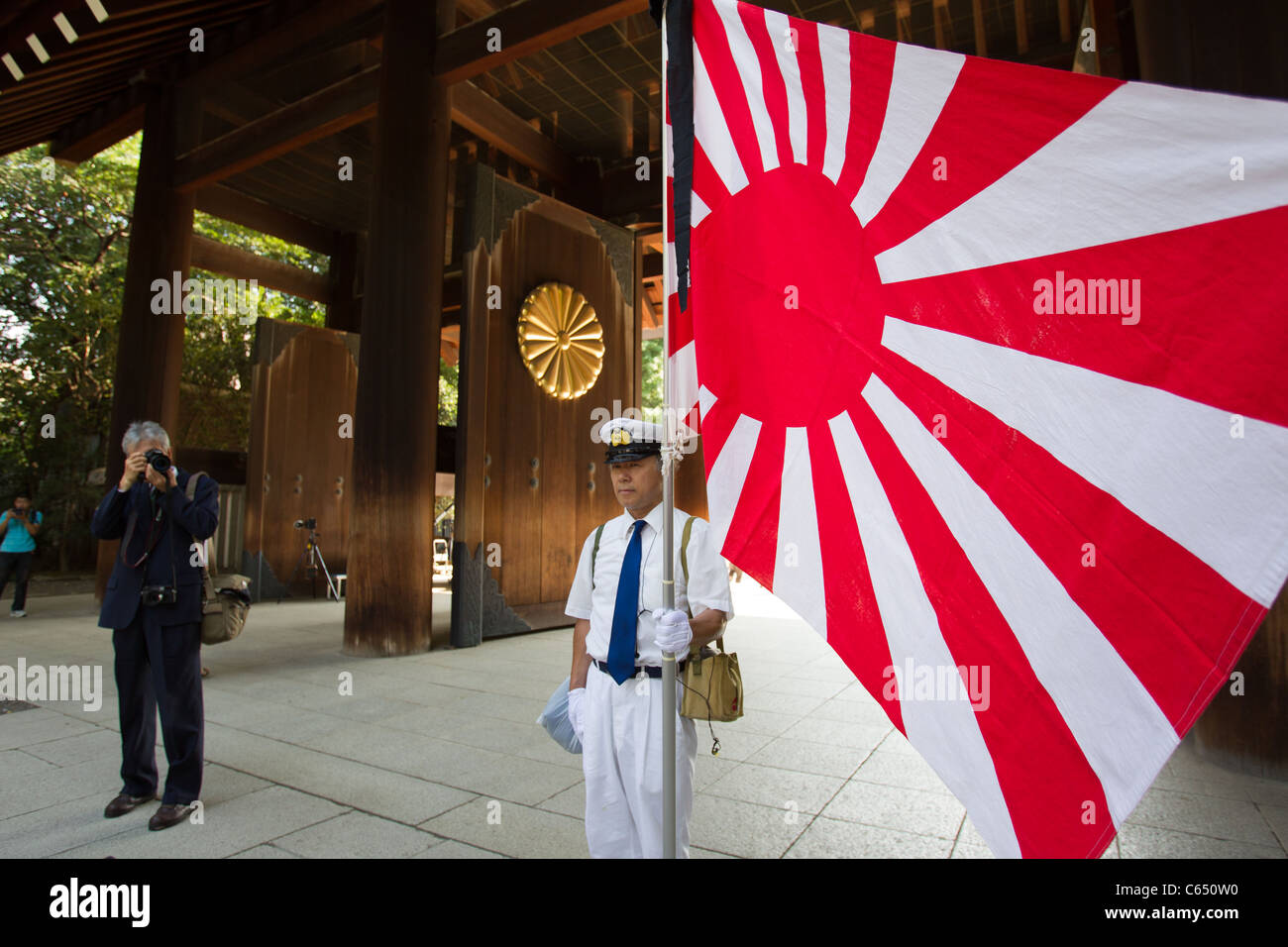 A man dressed in a Japanese military uniform proudly holds up the flag of Japan at Yasukuni Shrine. Stock Photo