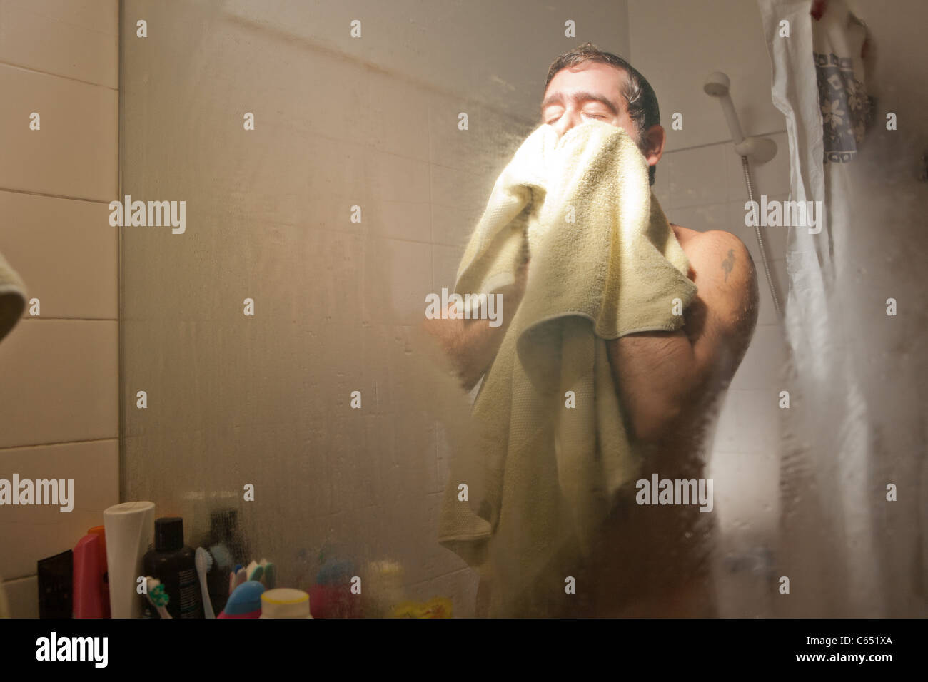 A man drying his face with a towel after a shower in a bathroom Stock
