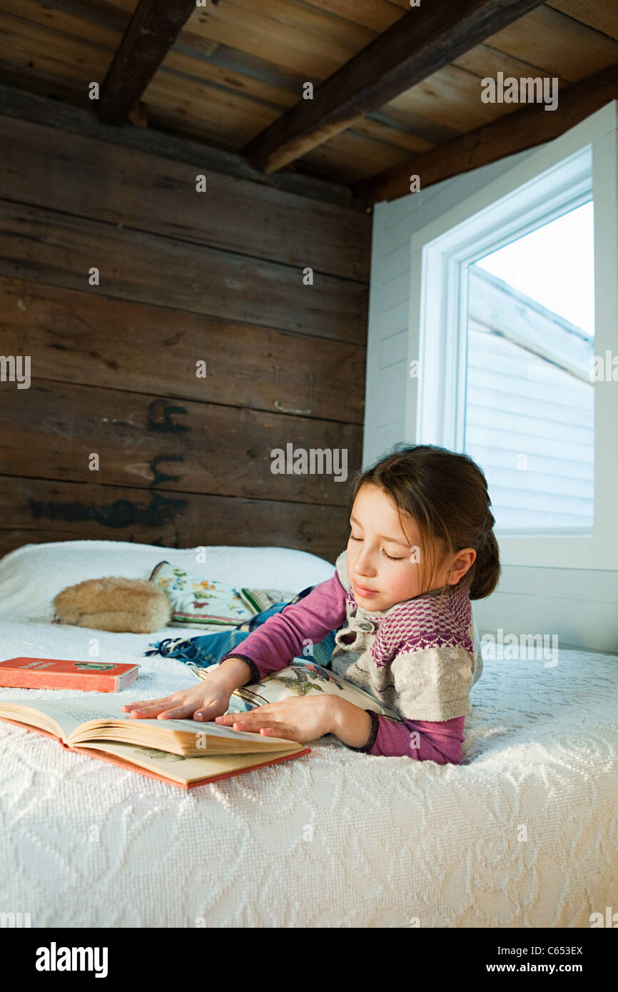 Young girl lying on bed reading book Stock Photo