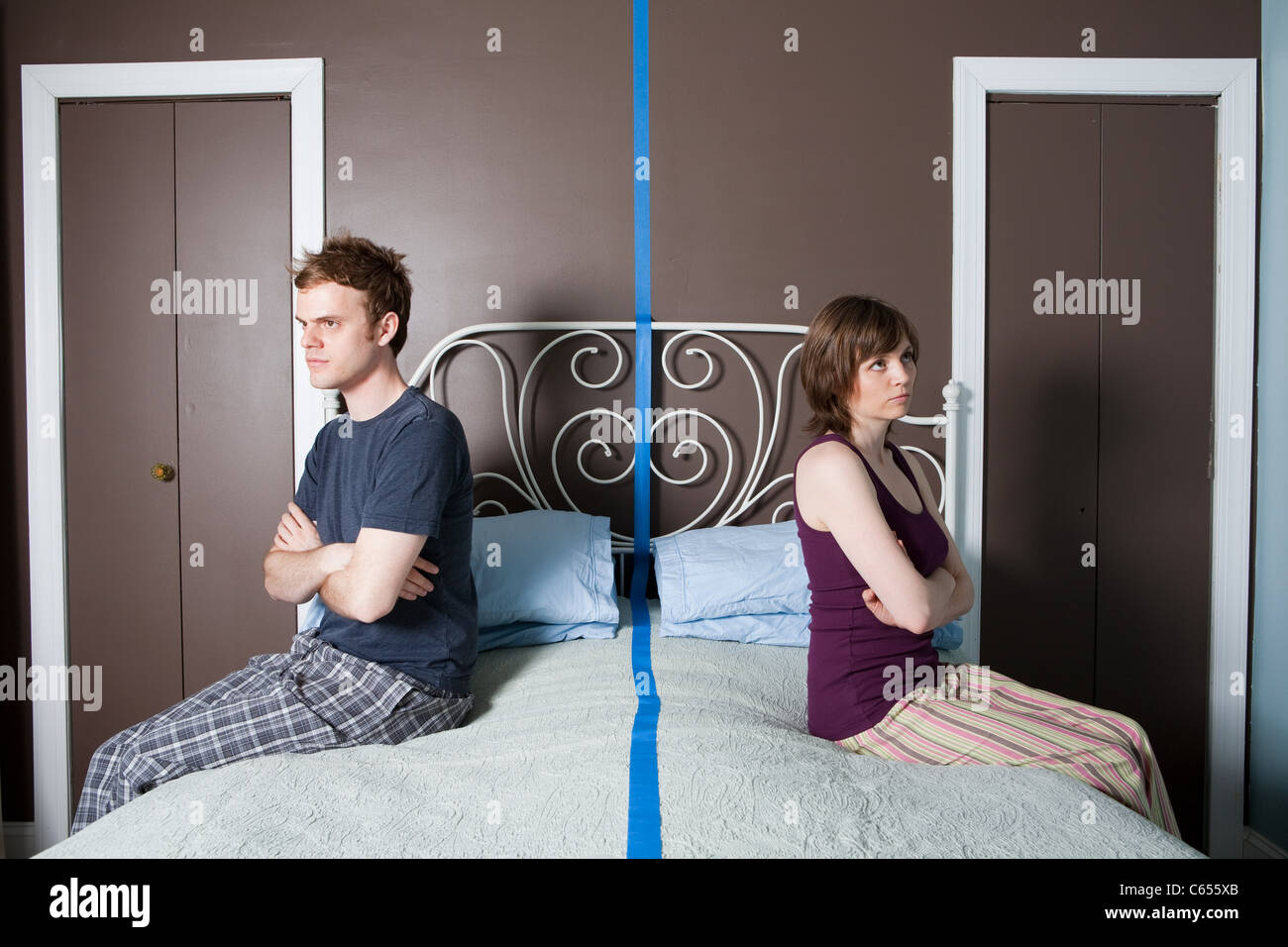 Young couple sitting on bed separated by blue line Stock Photo