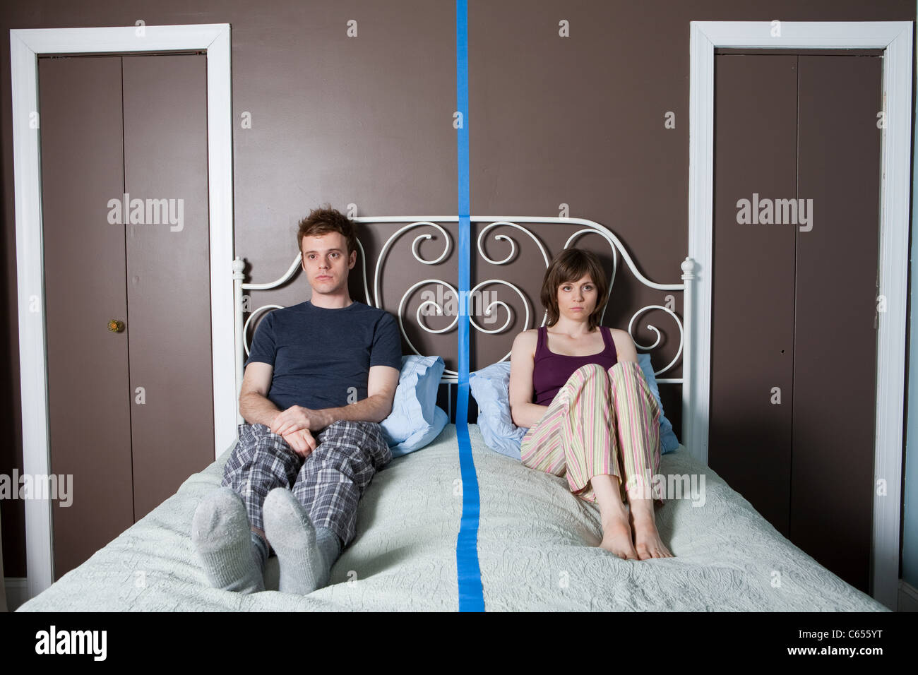 Young couple sitting on bed separated by blue line Stock Photo