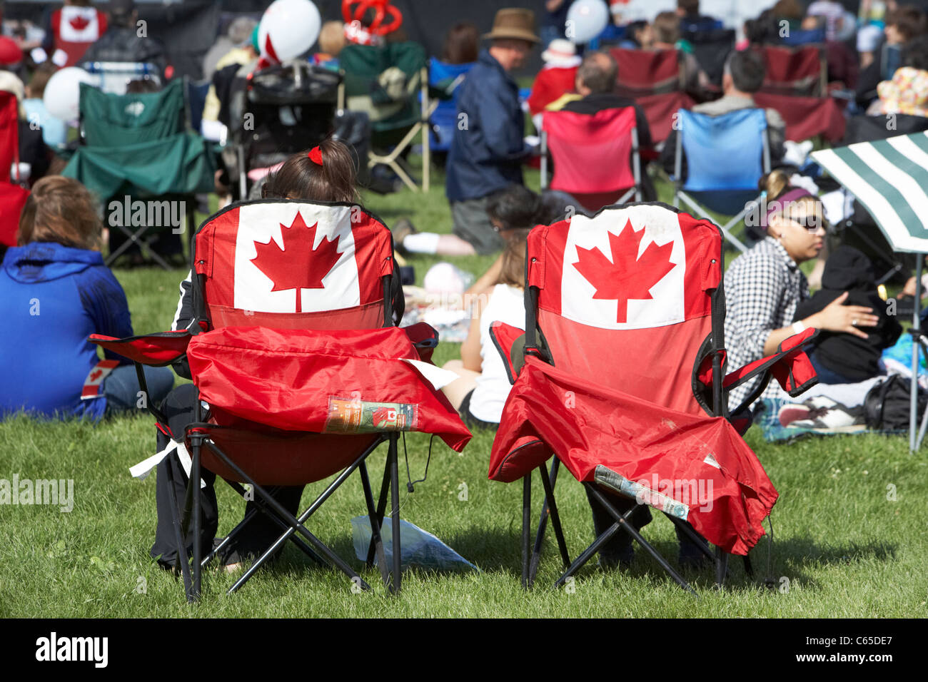 people sitting in maple leaf chairs in the crowd at festival on canada day Saskatoon Saskatchewan Canada Stock Photo