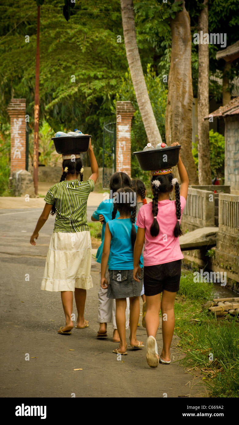 Balinese girls carrying bowls of empty plastic bottles on heads Stock