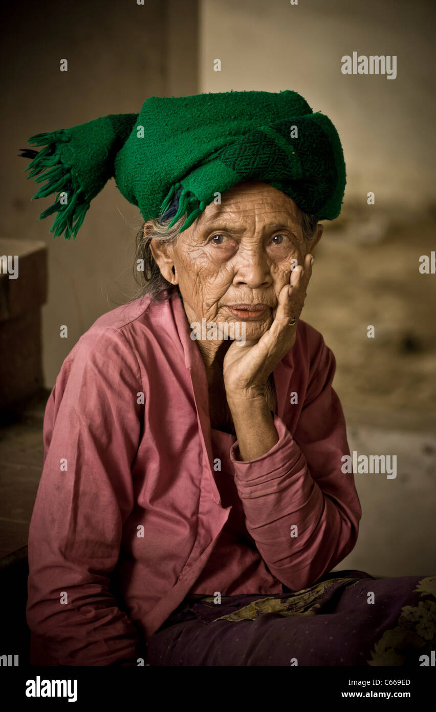 Old Balinese woman wearing a green scarf around her head, sitting outside a shack Stock Photo