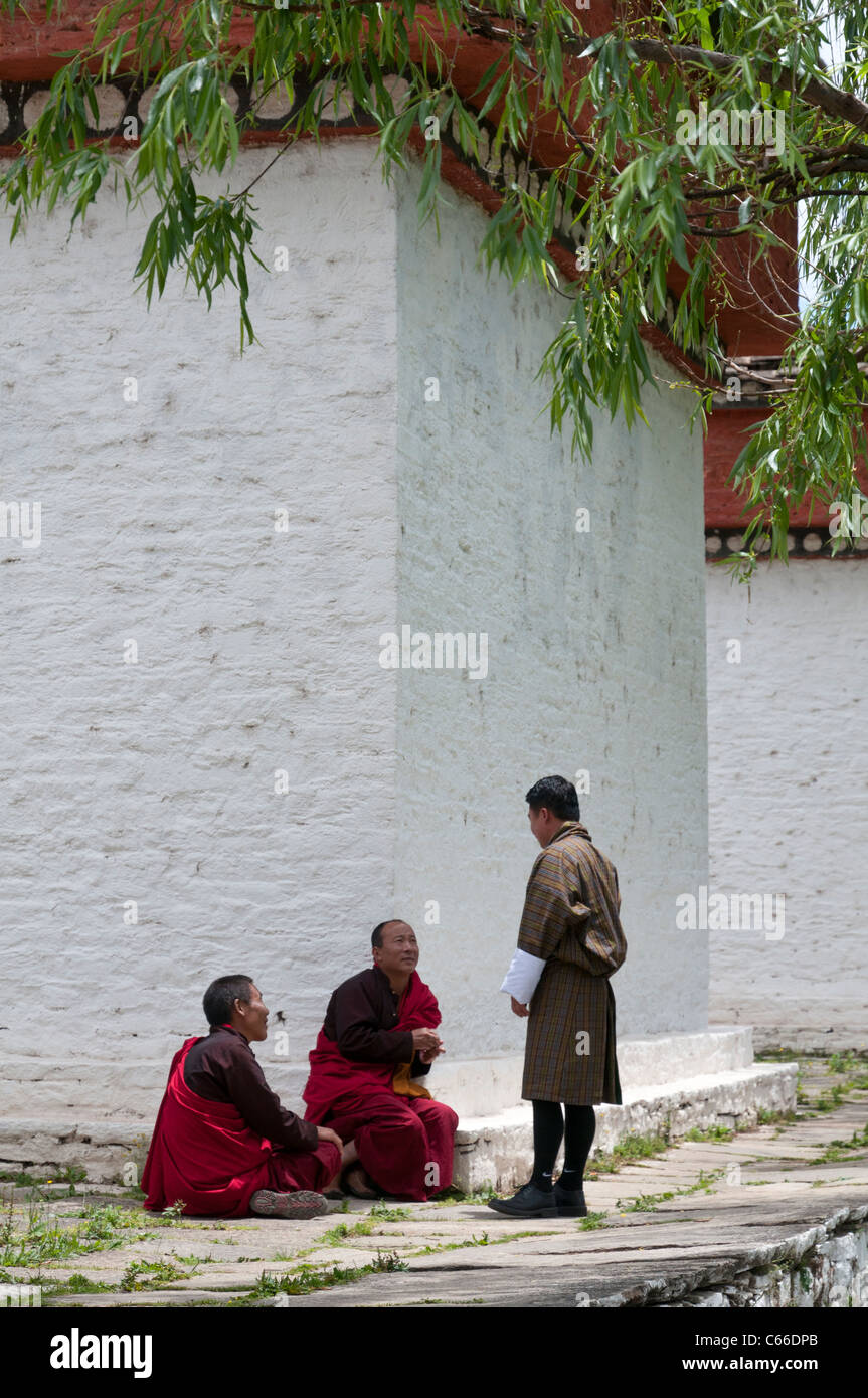 2 monks and man in gho talking at chorten. Paro. Bhutan Stock Photo