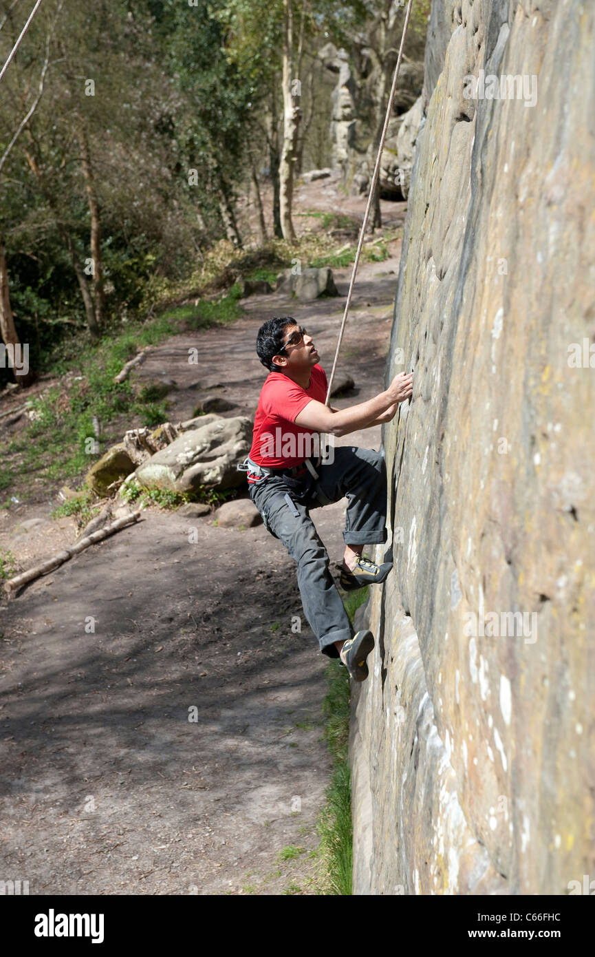 Male rock climber ascends a near vertical wall at Harrison's Rocks in Kent, UK, as he is belayed by his partner below. Stock Photo