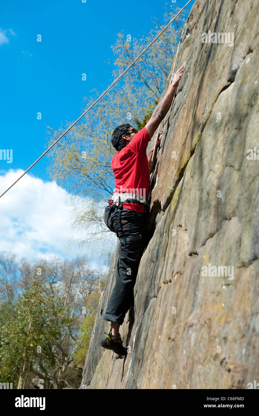 Male rock climber ascends a near vertical wall at Harrison's Rocks in Kent, UK, as he is belayed by his partner below. Stock Photo