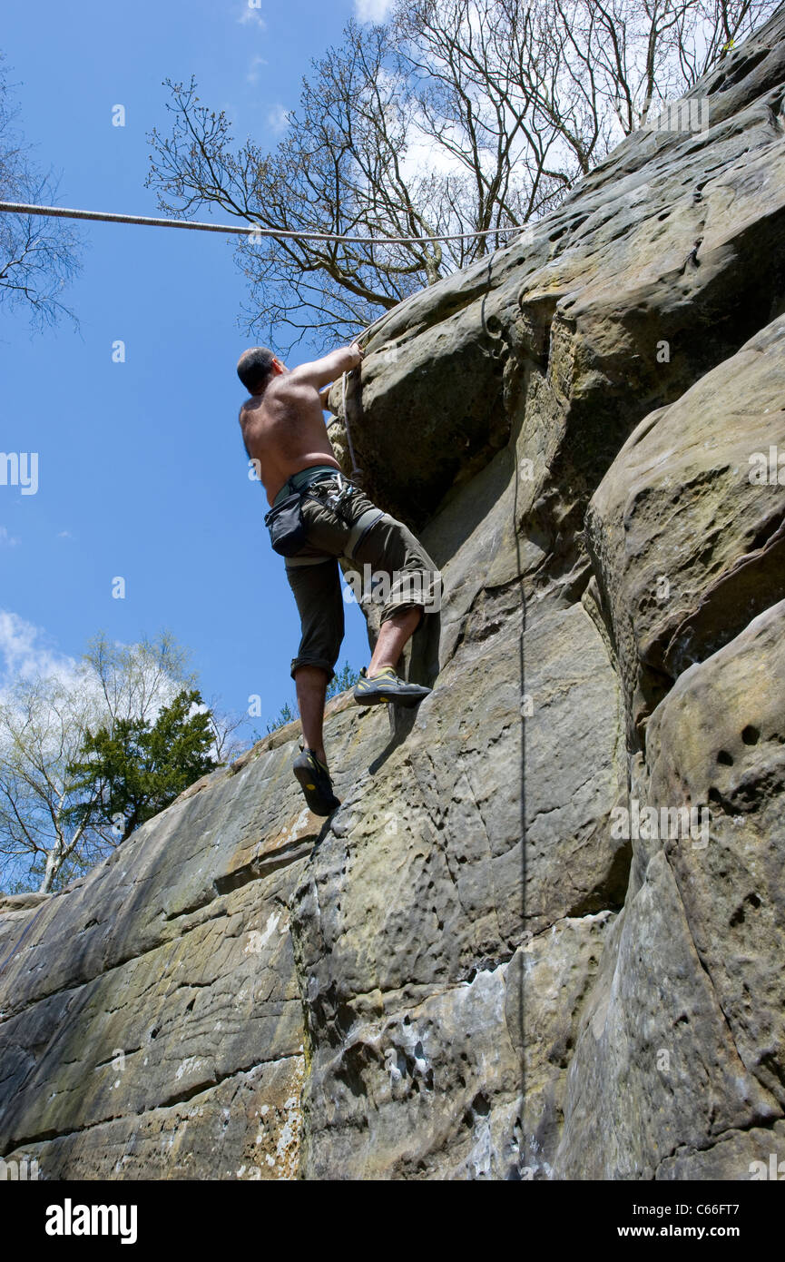 An adult male rock climber tackles an overhang at Harrison's Rocks in Kent, UK, while being belayed from below by his partner. Stock Photo