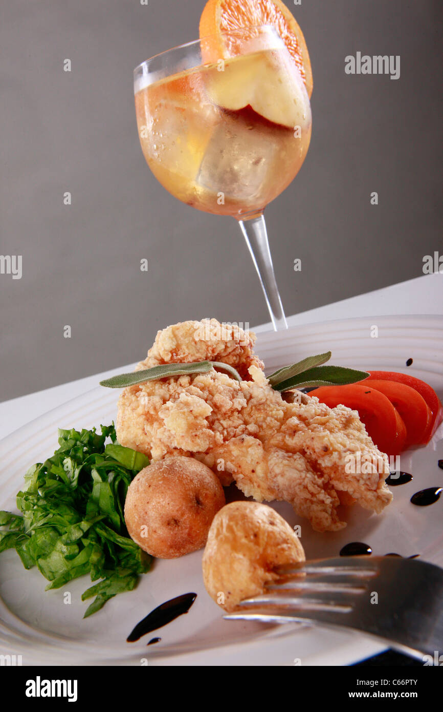 Crisp battered fish, mini potatoes, sliced tomato, and spinach julienne with white sangria Stock Photo