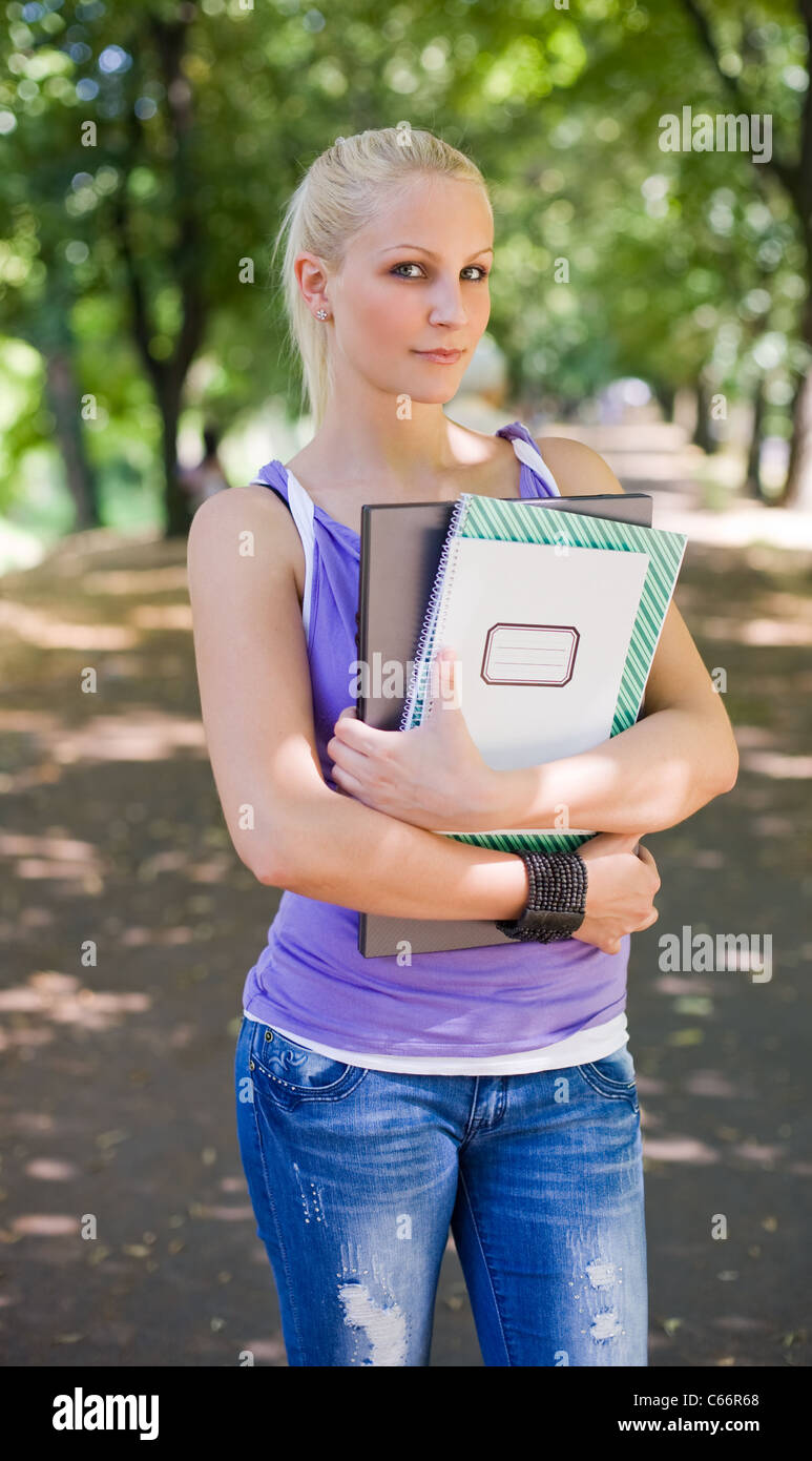 Beautiful firendly blond student girl holding exercise books and laptop ...