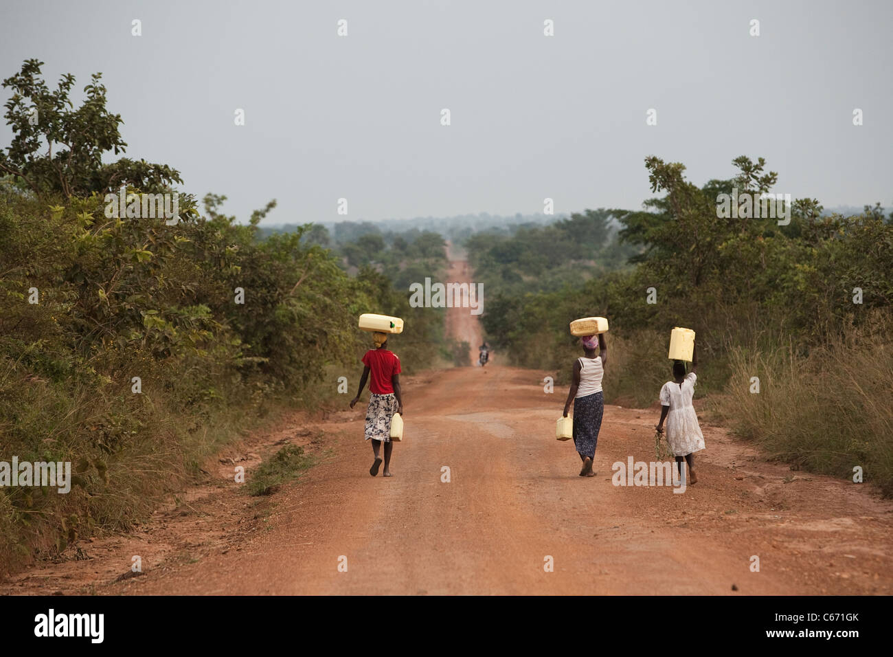 Women carry water along the road from Soroti to Amuria Town. Amuria District, Uganda, East Africa Stock Photo