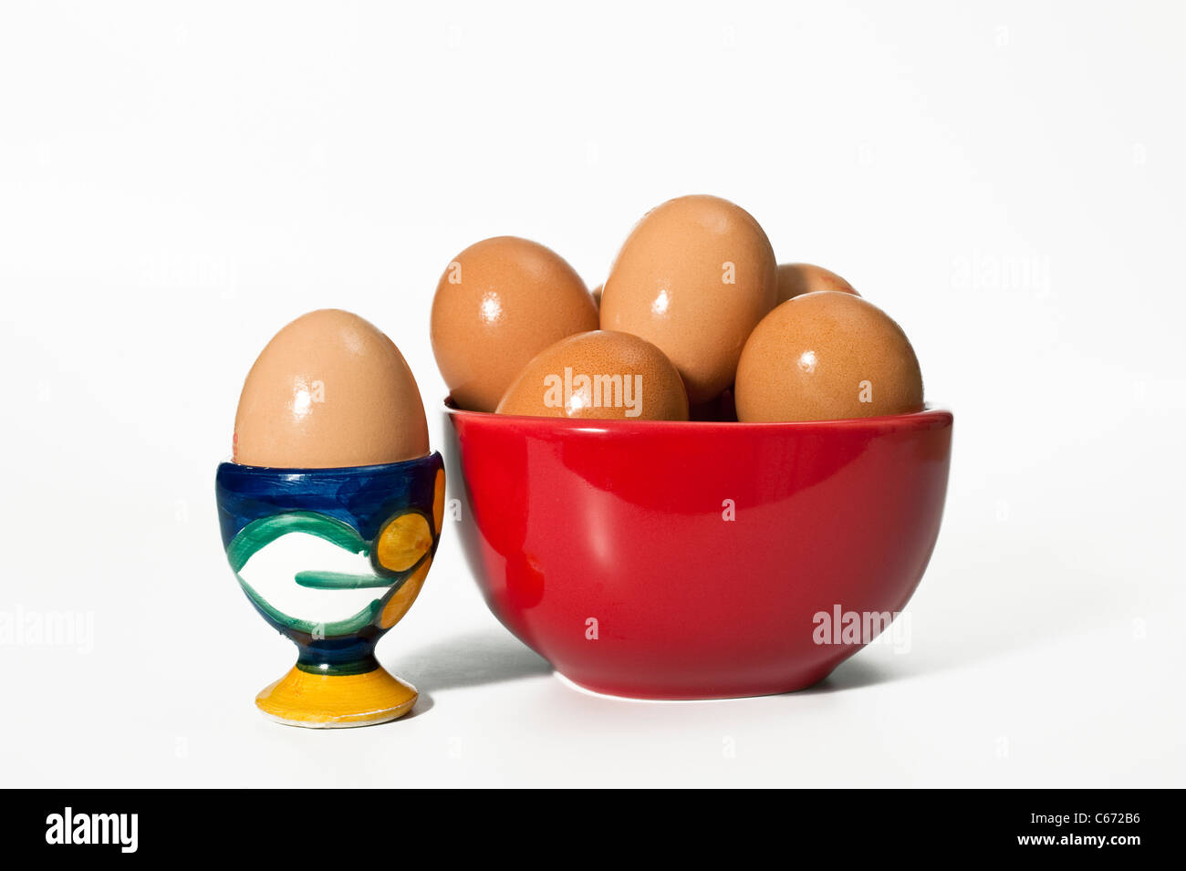 A Boiled egg in an eggcup with other eggs in a red bowl Stock Photo