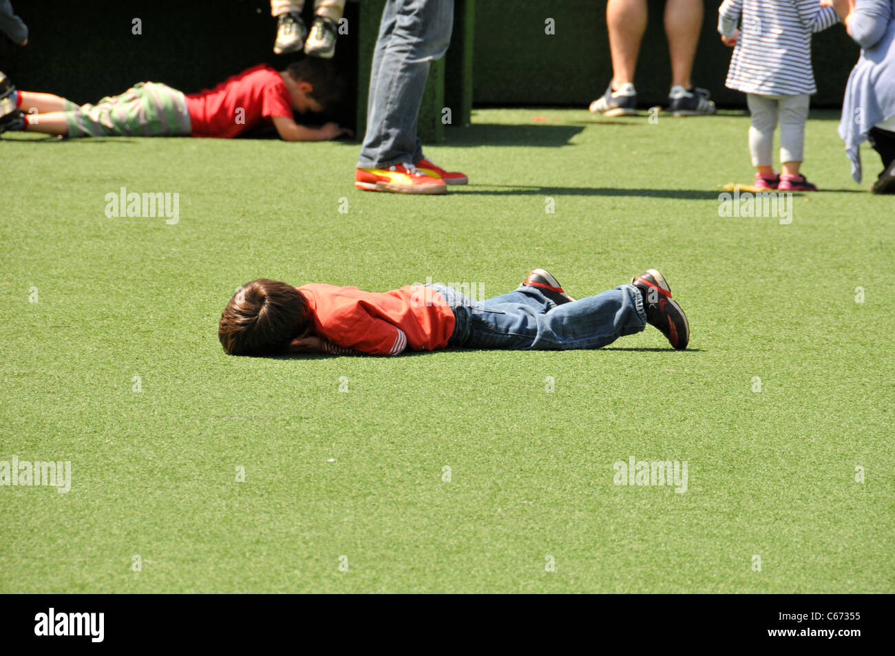 Lonely child alone separated sad ignored child playing lying face down having fun sunny day London Stock Photo