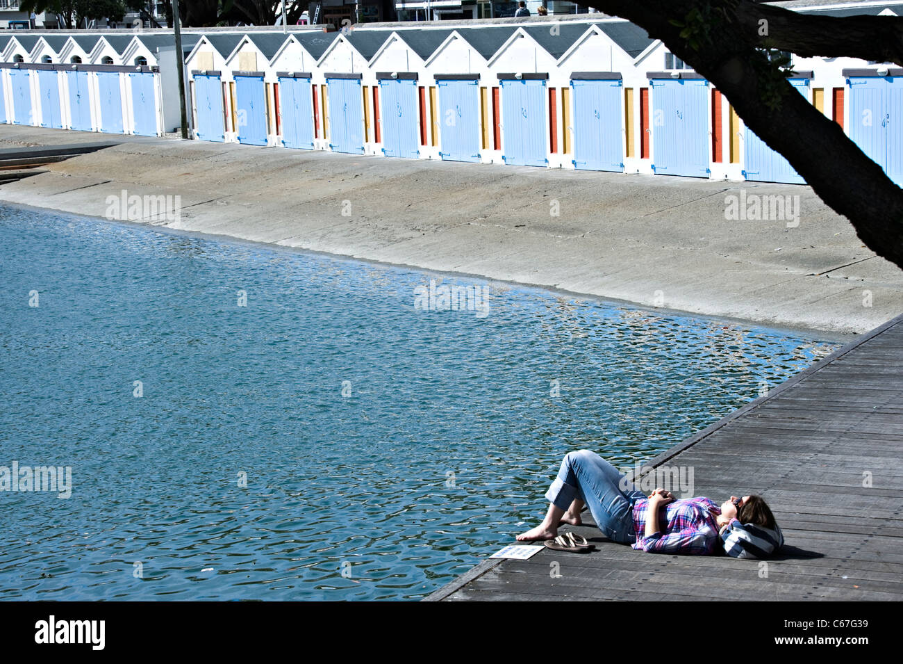 Girl Sunbathing by a  Line of Boat Sheds at The Royal Port Nicholson Yacht Club Wellington North Island New Zealand NZ Stock Photo