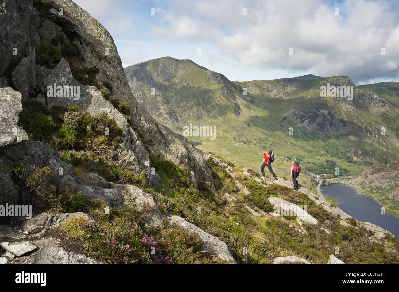 Hikers climb mount Tryfan north ridge above Llyn Ogwen lake in mountains of Snowdonia with Y Garn beyond Ogwen Valley North Wales UK Stock Photo