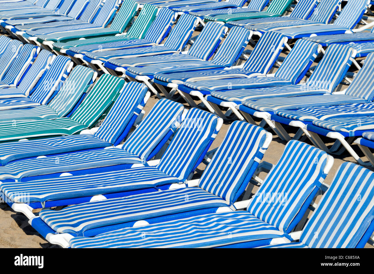 Blue and white striped padded sunbeds packed together on a beach Stock Photo