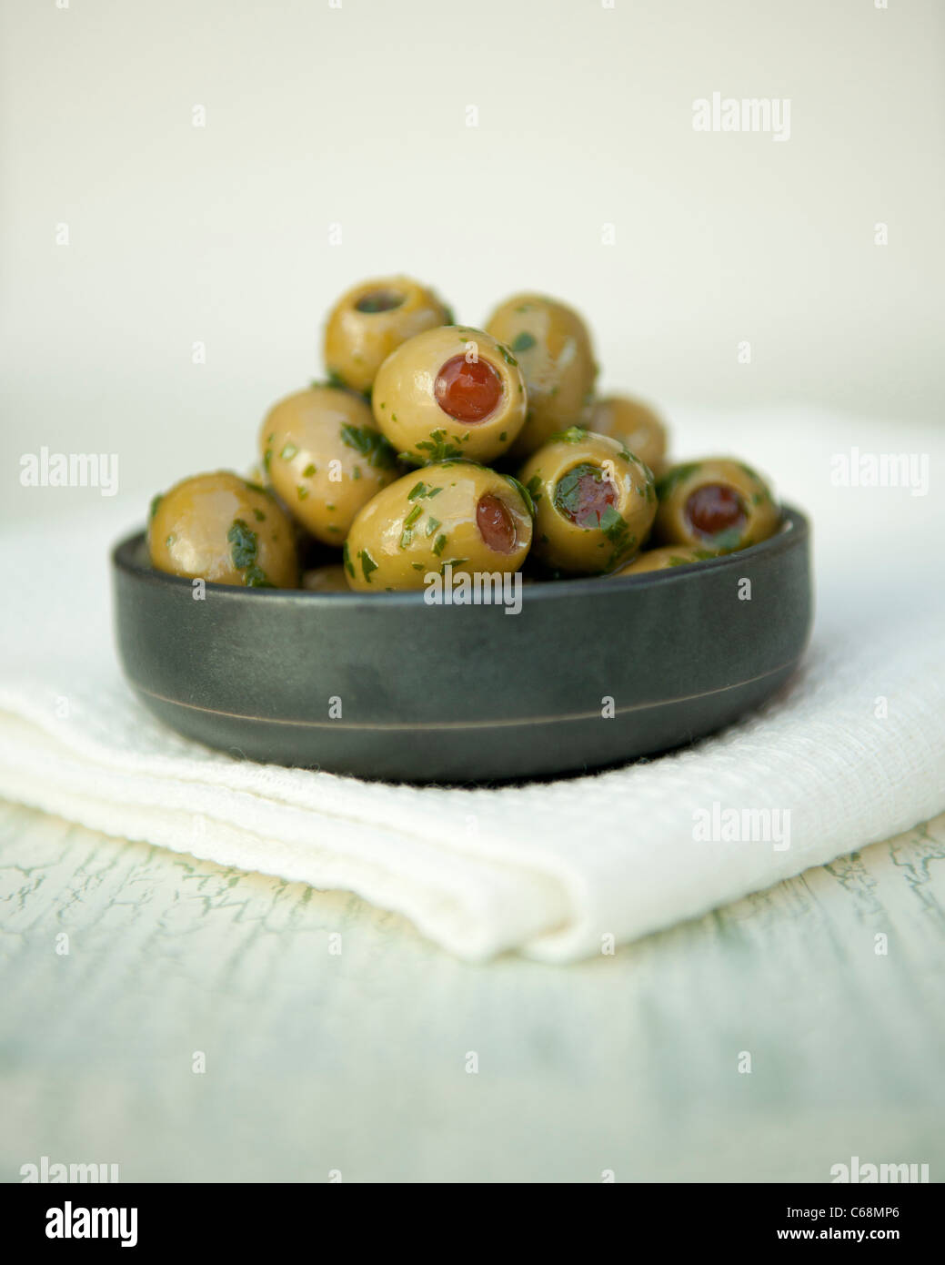 Green olives stuffed with red peppers with olive oil and herbs in a pot