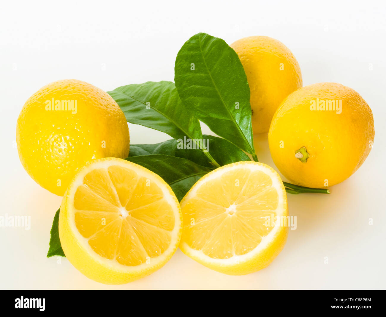 drei Zitronen mit Blättern, davor liegt eine aufgeschnittene Zitrone | three lemons with leaves, in front is a cut lemon Stock Photo