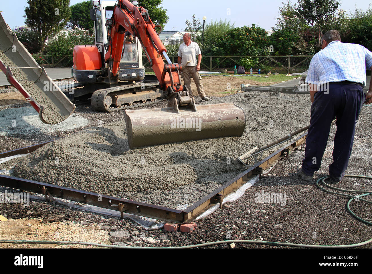 Pouring fresh mixed concrete from delivery lorry onto prepared ground for caravan base. Stock Photo