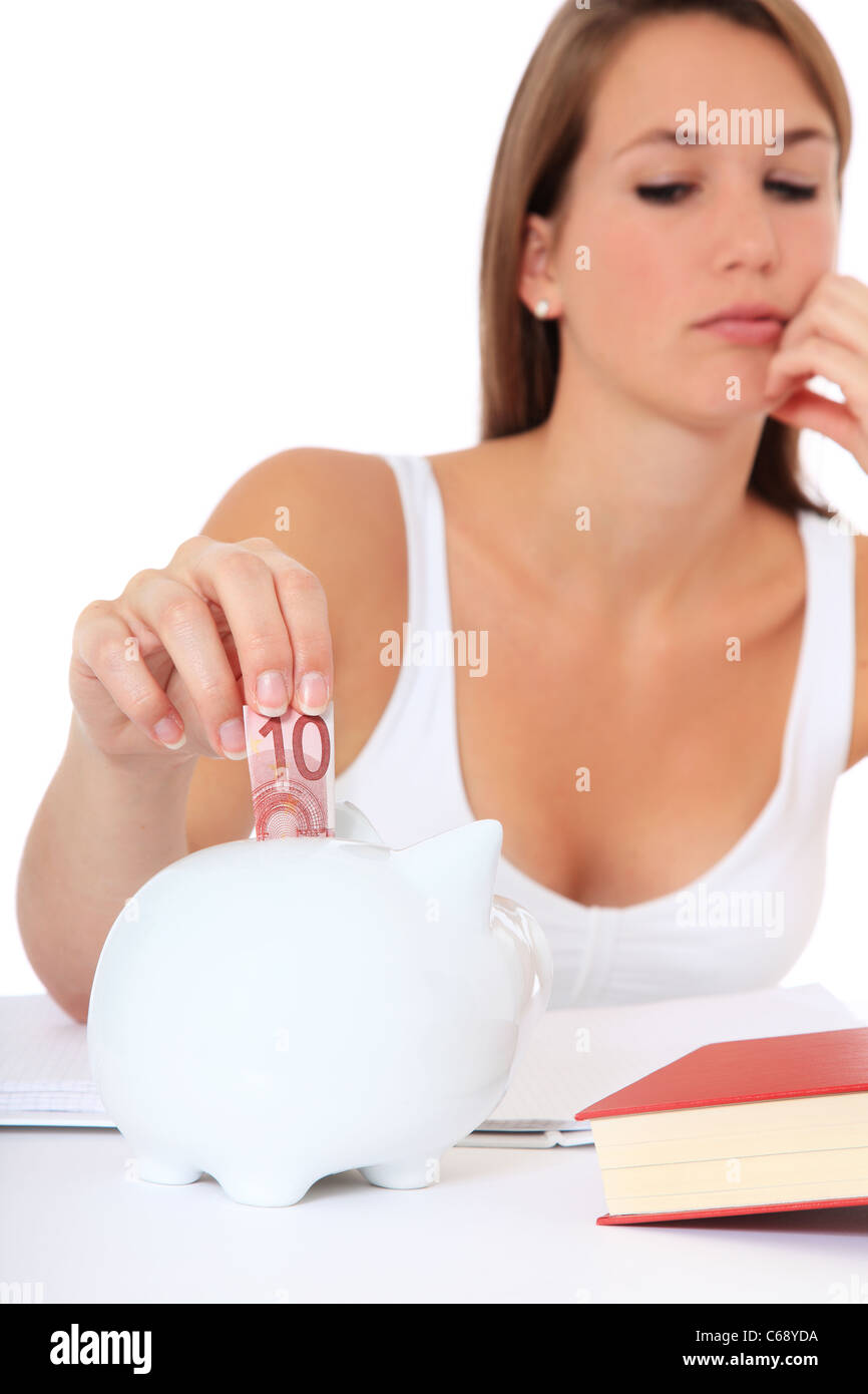 Attractive young student puts money in her piggy bank. All on white background. Stock Photo