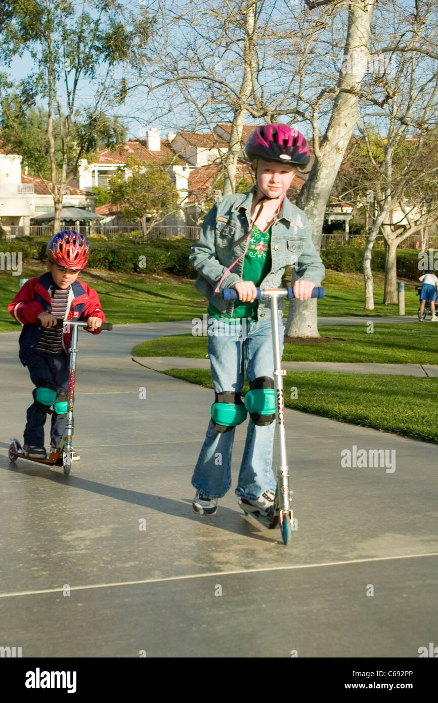 Wearing jacket Young girl 6-7 year old and pre-K Hispanic boy 4-5 years old on scooters at park. MR © Myrleen Pearson Stock Photo