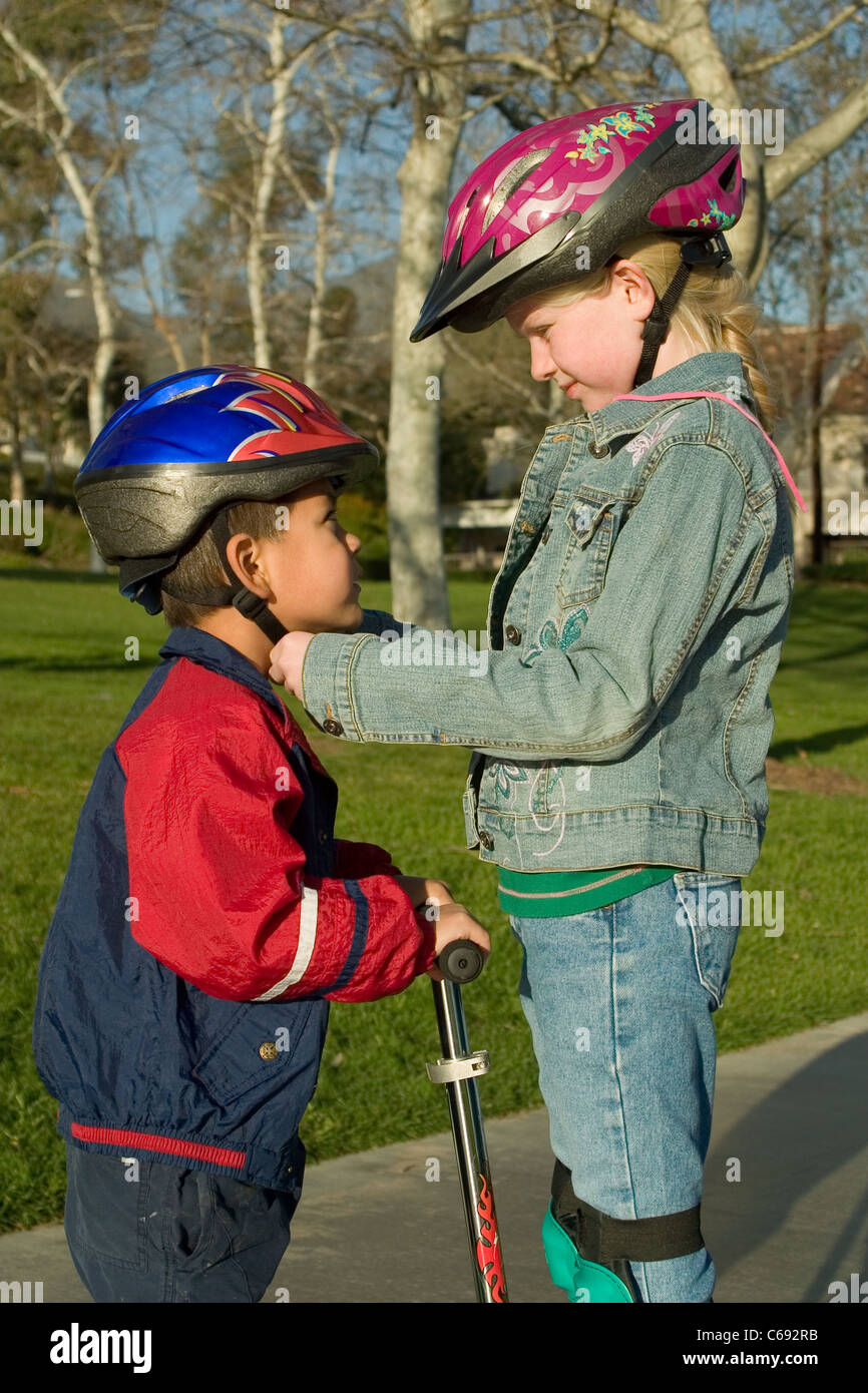 Ethnic diversity diverse adoption Young girl  7-8 year old fastens helmet for pre-K adopted Hispanic brother. MR © Myrleen Pearson Stock Photo