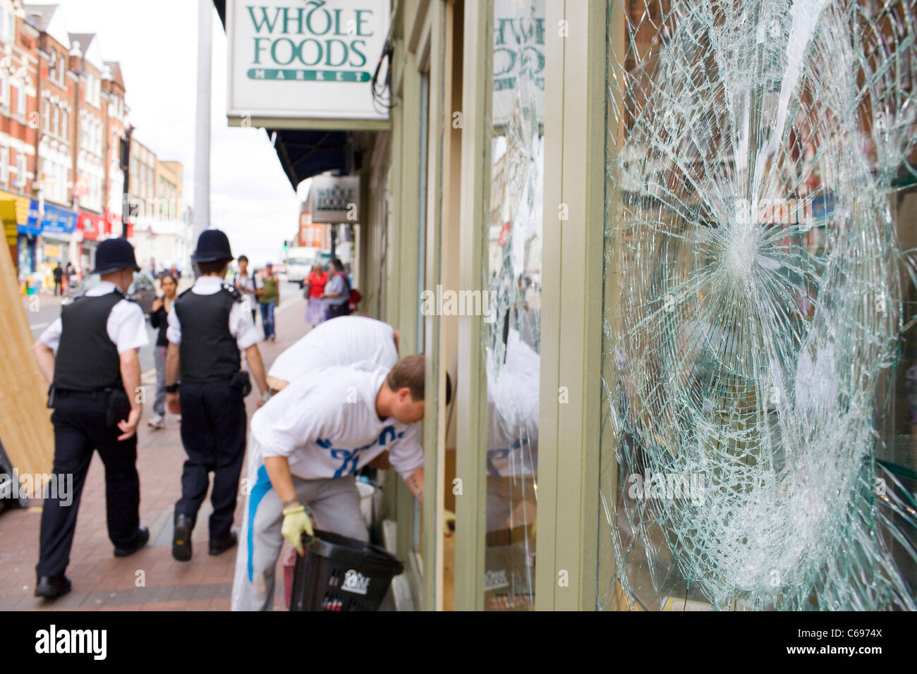 London police walk past smashed shop windows in Clapham damaged in the London August riot. Stock Photo