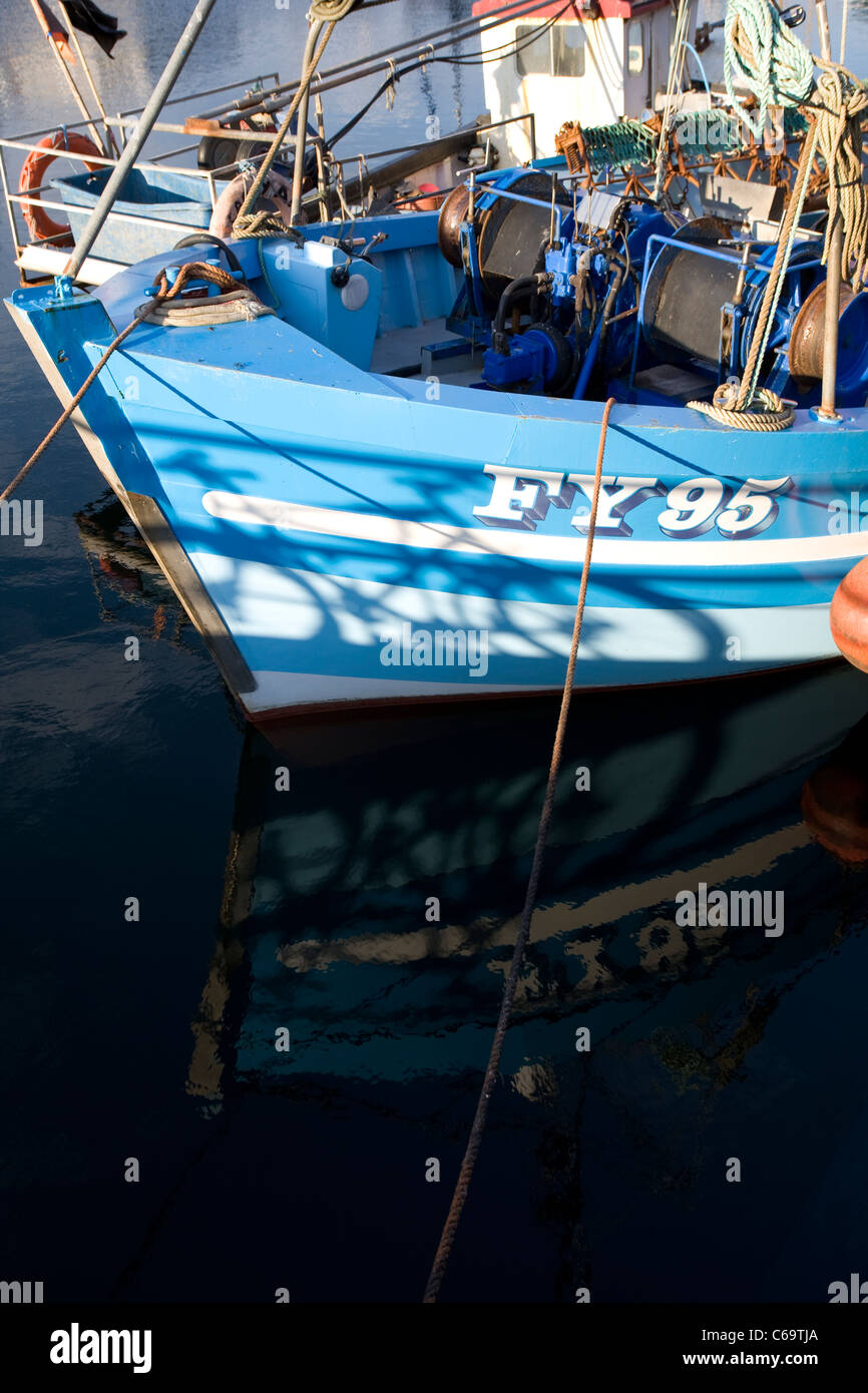 The blue and white hull of FY95 fishing boat reflected in the water at ...