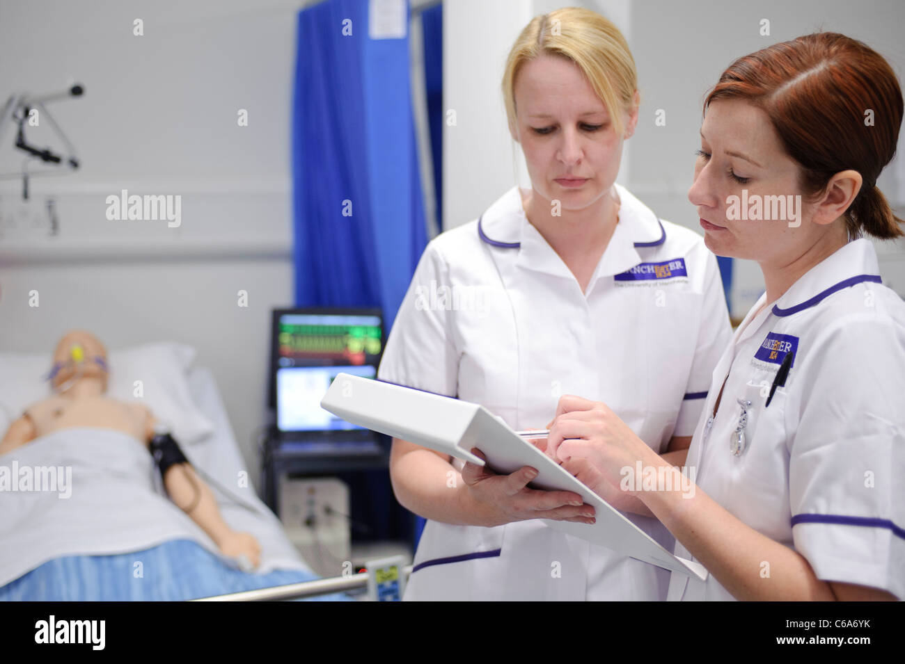 student nursing nurses reading patient chart by dummy patient in clinical skills lab hospital setting Stock Photo