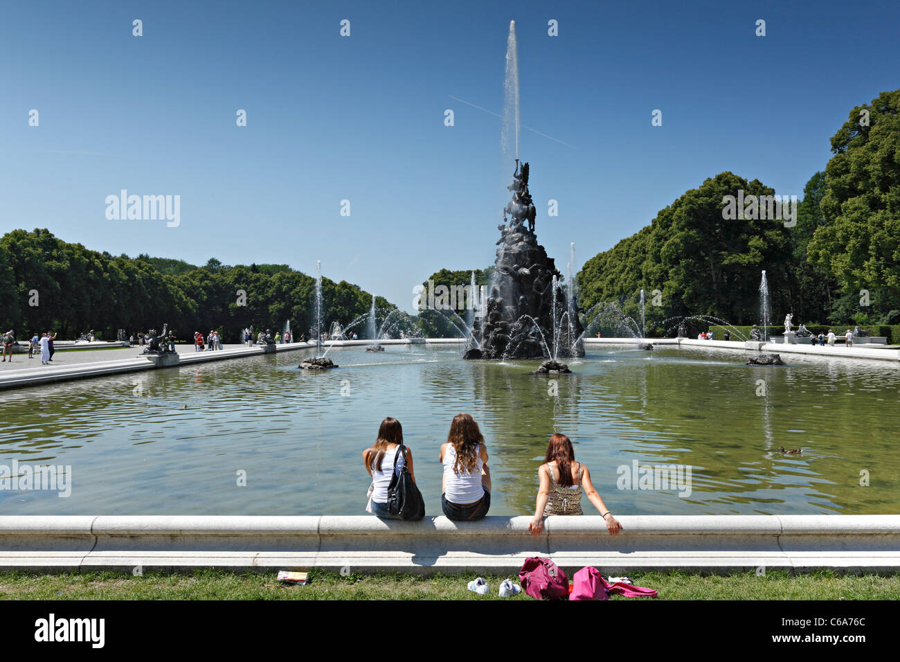 3 young woman sitting on the edge of Fama Fountain, Herreninsel Upper Bavaria Germany Stock Photo