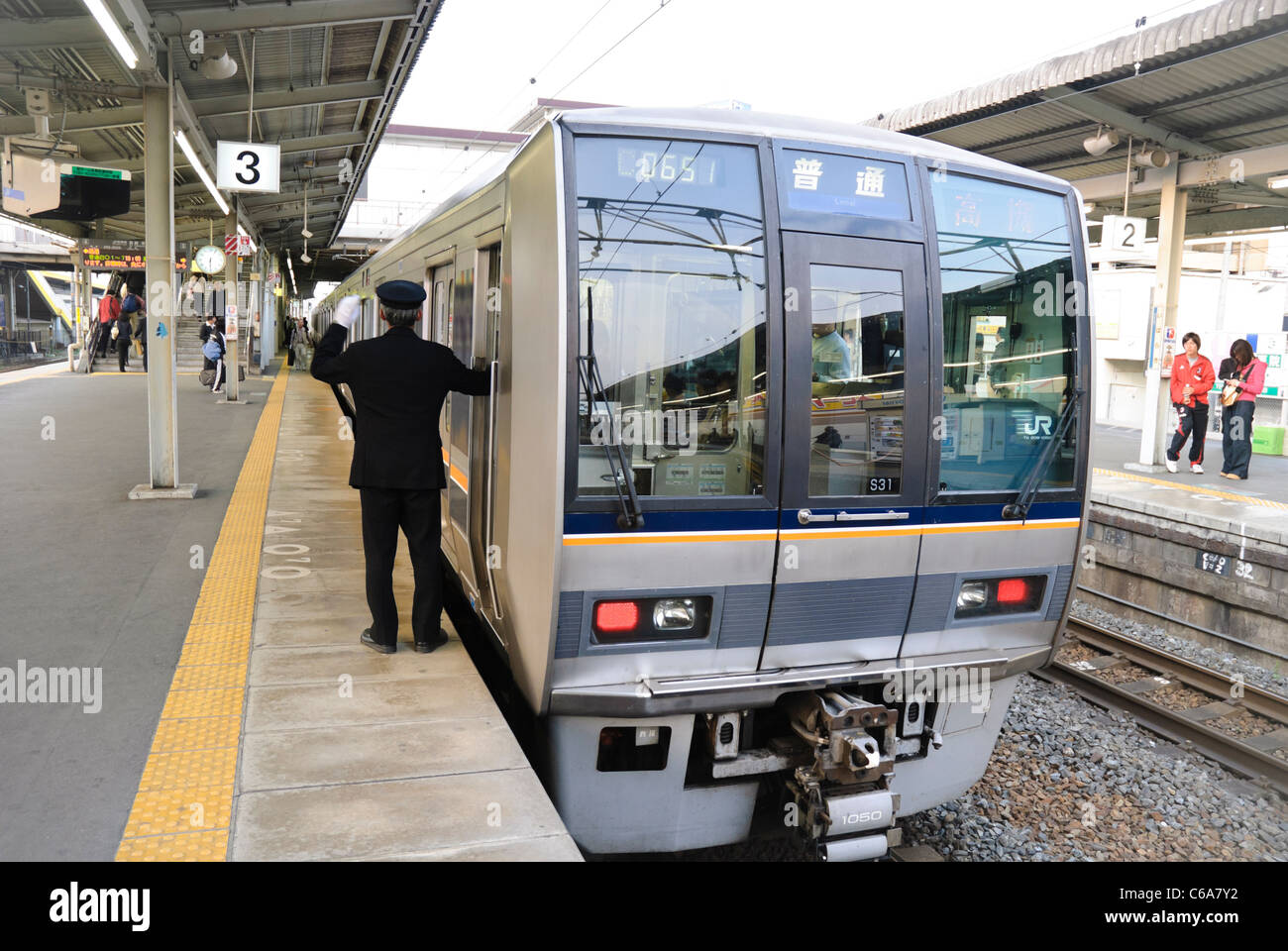Guard of a Japanese commuter train signals the driver that it's safe to depart. Passenger train, Japan. Stock Photo