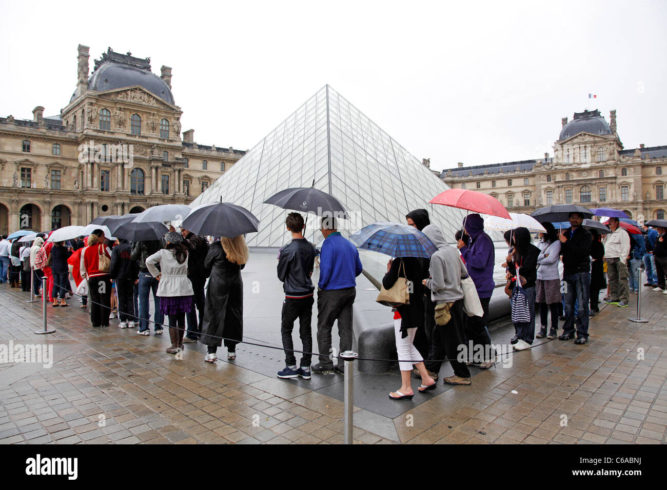 Tourists queuing in the rain at the Louvre Pyramid in Paris, France Stock Photo