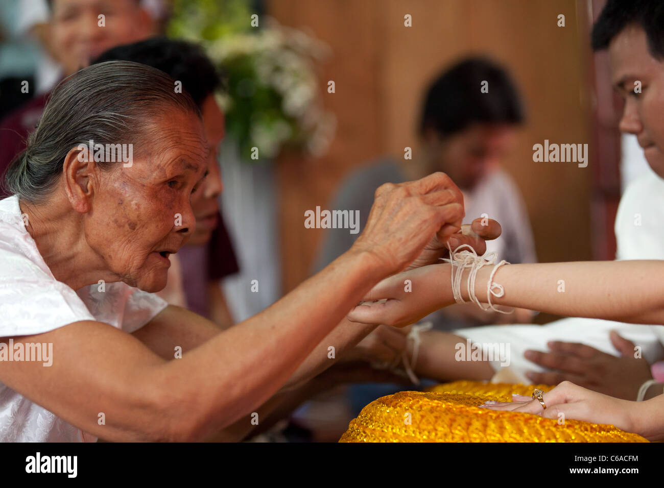 senior thai woman tie string around husband arm for buddhism religious C6ACFM