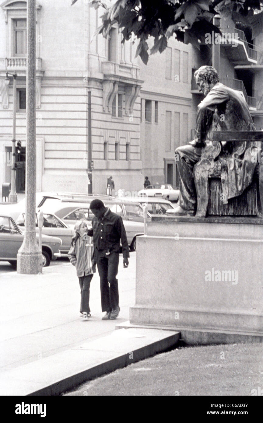 black teenager with arm over shoulder of  white friend walk past statue of Abraham Lincoln in the city of San Francisco Stock Photo