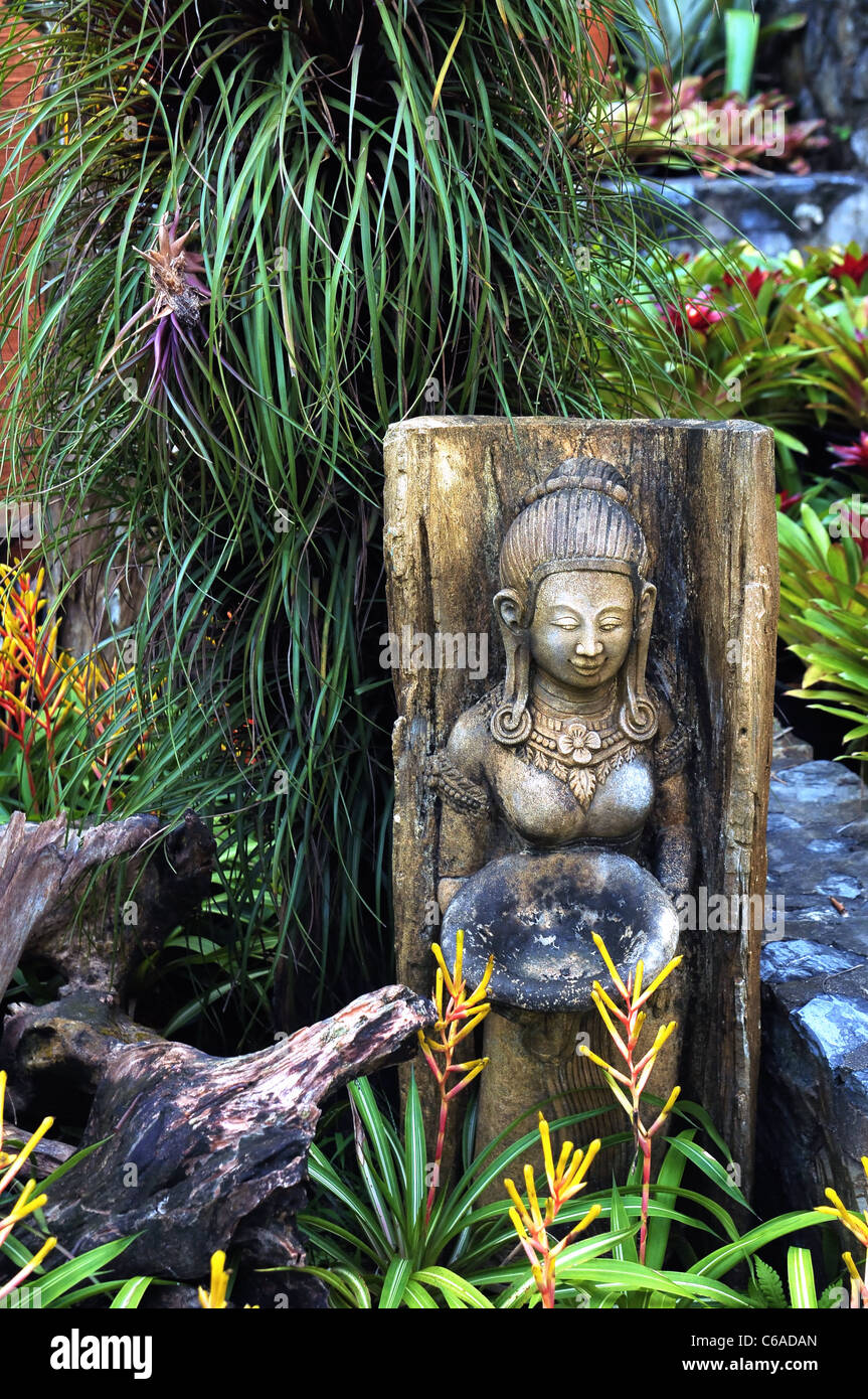 Statue of a buddhist goddess in the midst of green and colorful plants, stones and pottery Stock Photo