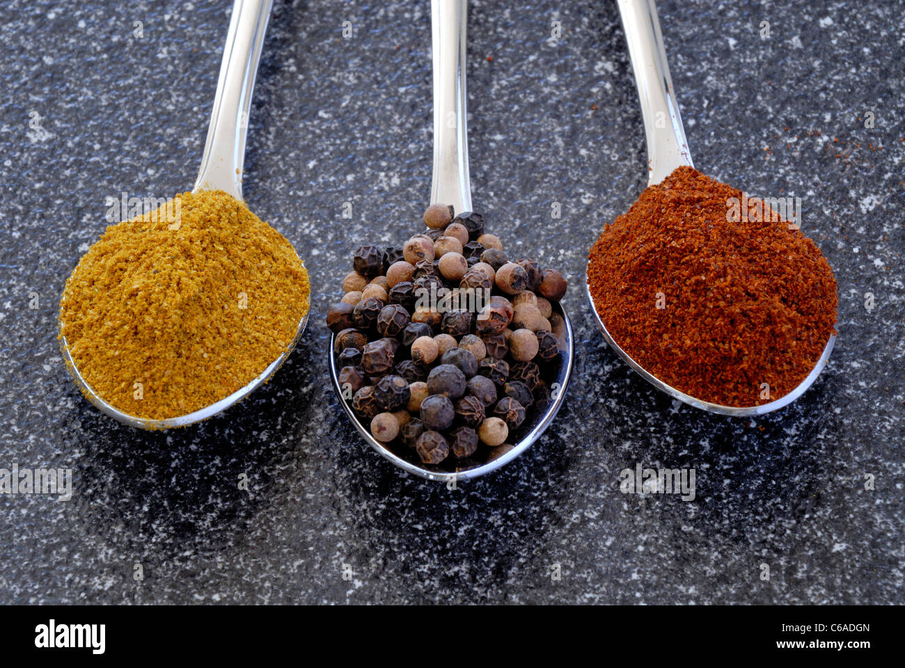 Three Teaspoons With Curry Powder, Black Peppercorns And Chili Powder