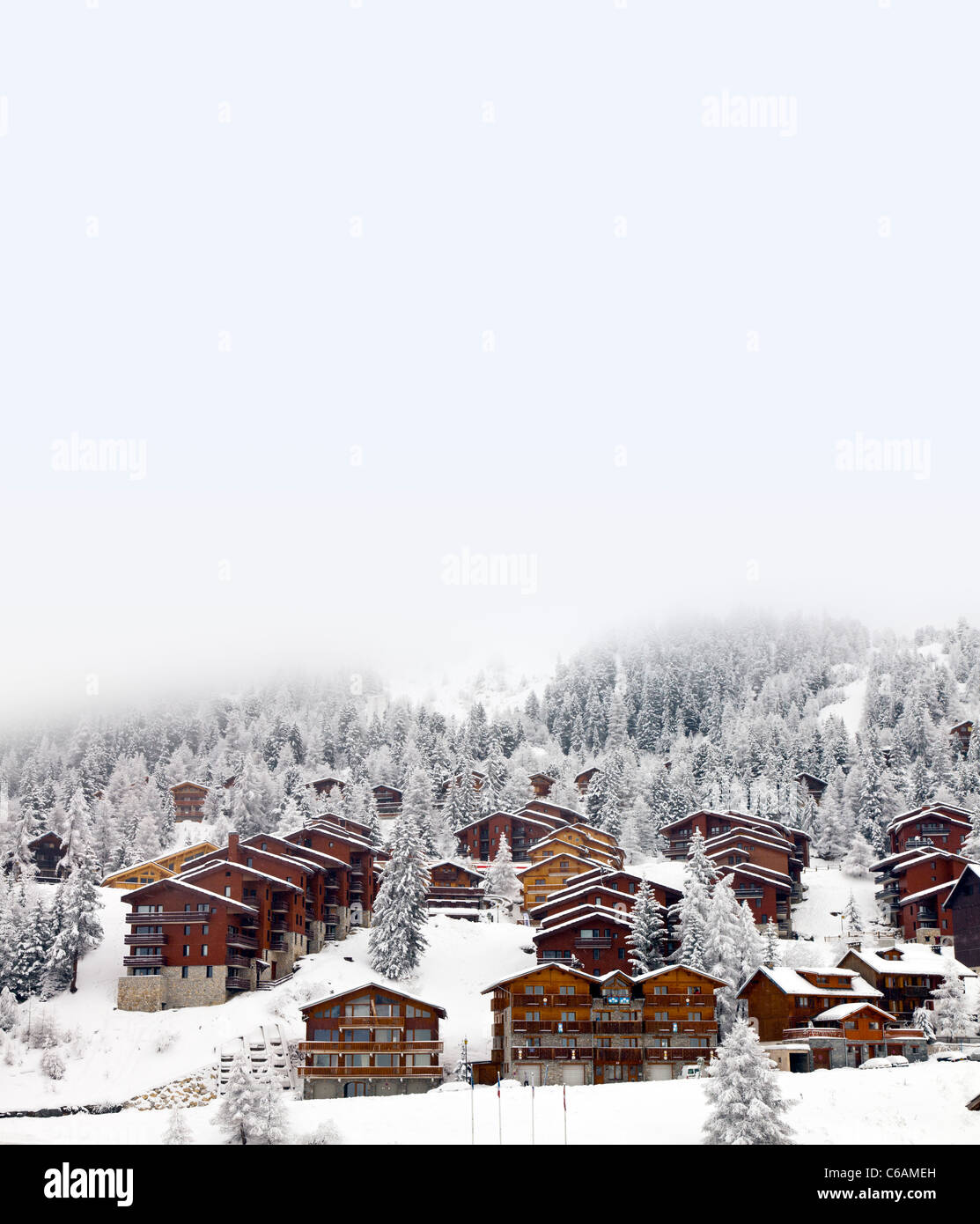 Fresh snow covered wooden ski chalets pine trees low cloud mist heavy white Stock Photo