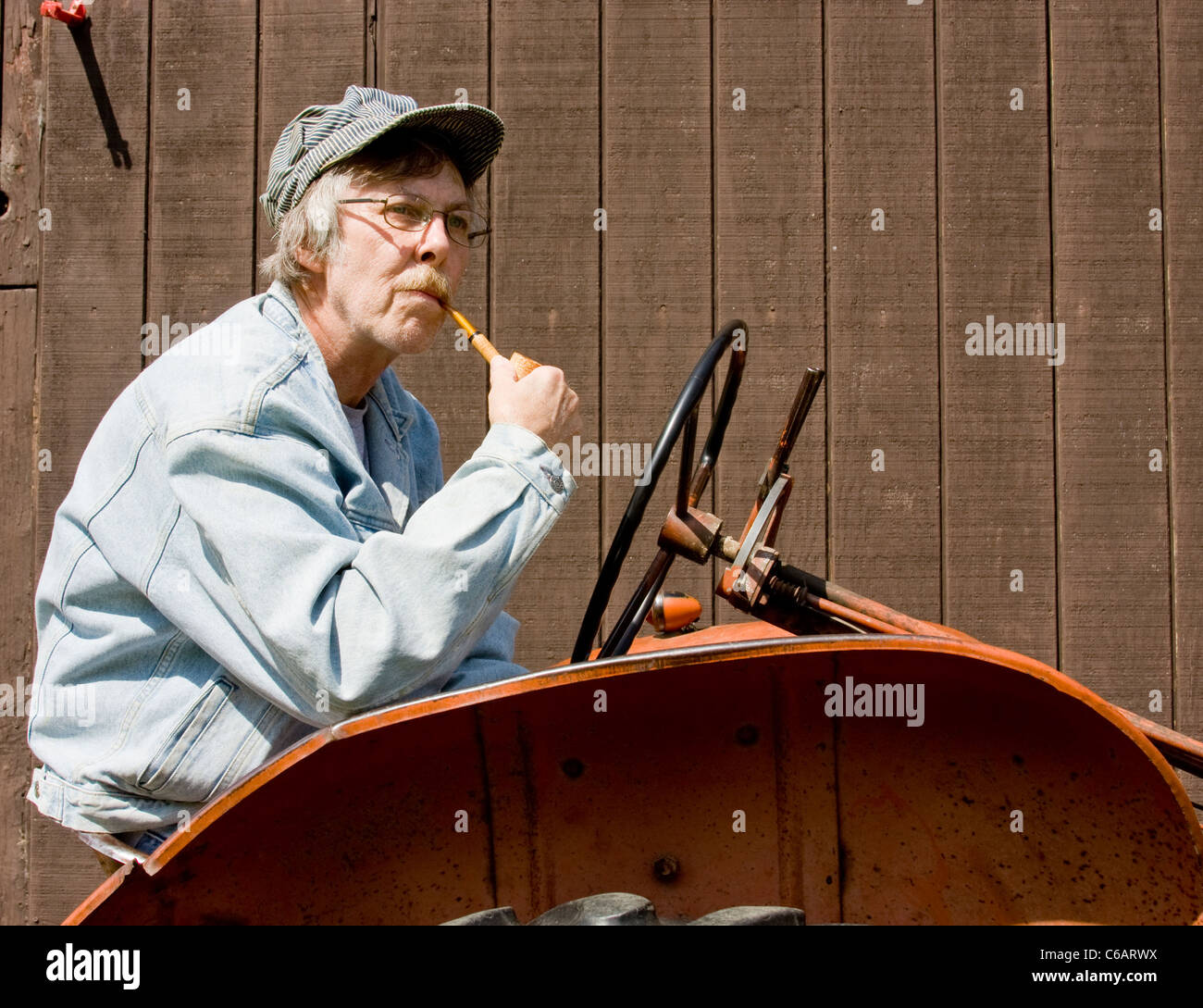 farmer smoking corn cob pipe sitting on a vintage tractor Stock Photo