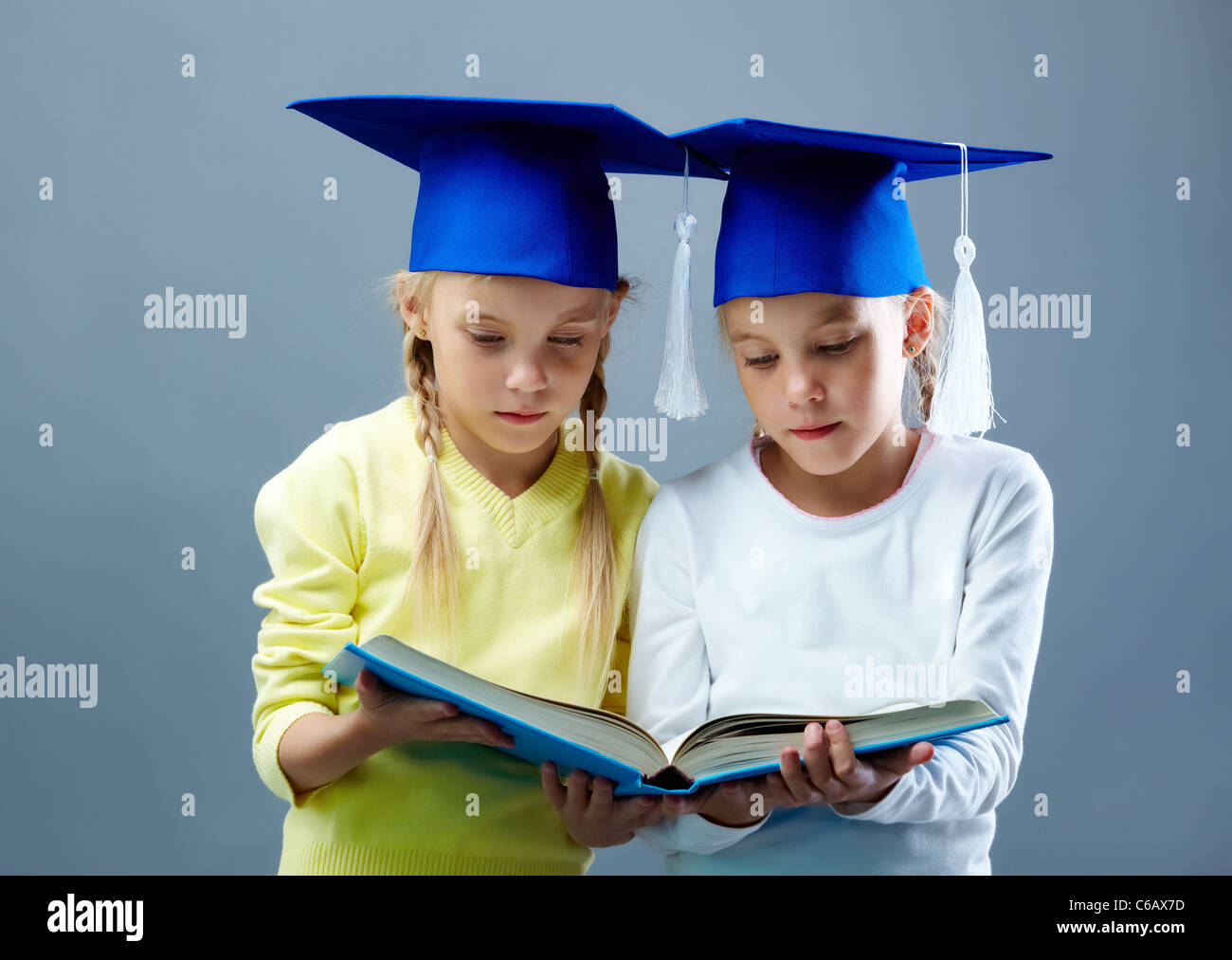 Portrait of lovely twin girls in hats with tassels reading book Stock Photo