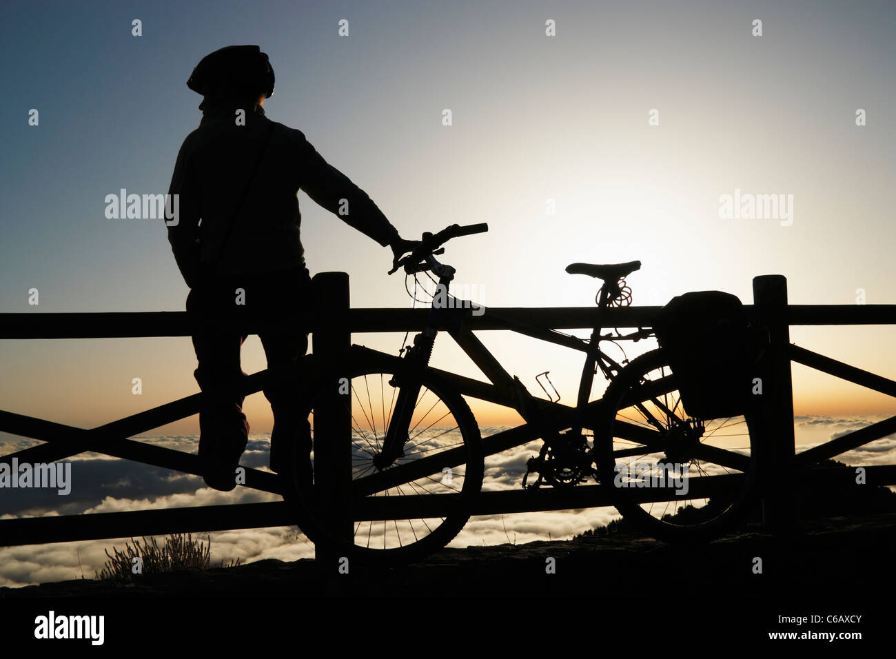 Woman with Mountain Bike above cloud layer at sunset at Pinos de Galdar on Gran Canaria, Canary Islands, Spain Stock Photo