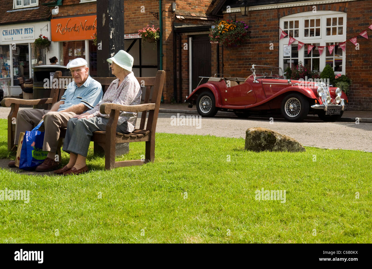 an elderly couple sitting on a public bench, a vintage MG classic car
