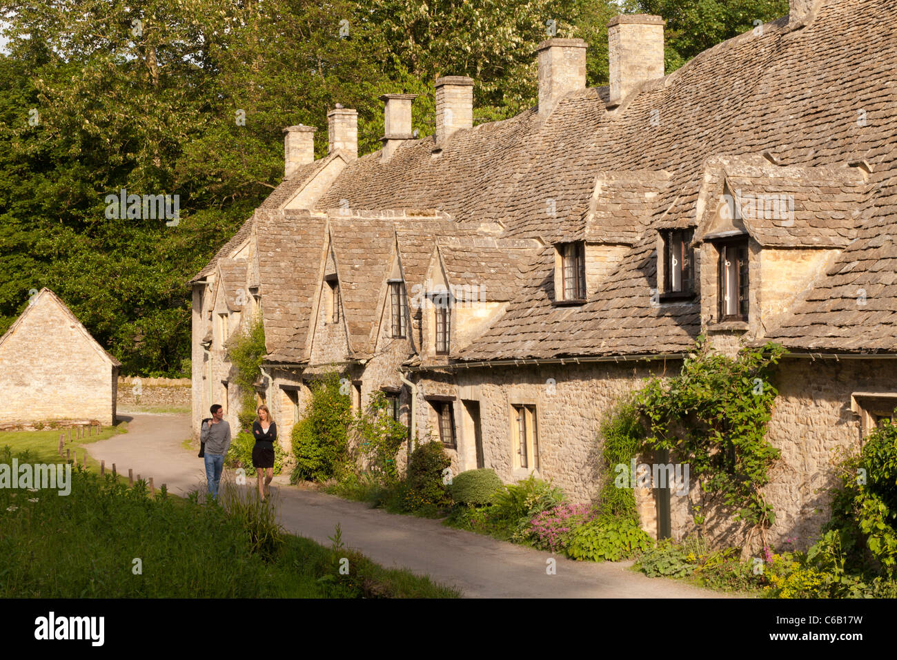 A young couple enjoy an evening stroll beside Arlington Row in the Cotswold village of Bibury, Gloucestershire UK Stock Photo