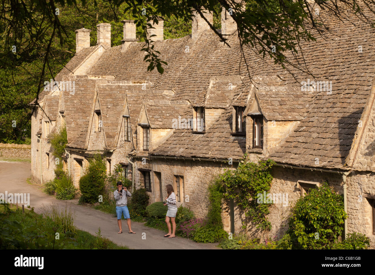 A young couple enjoy an evening stroll beside Arlington Row in the Cotswold village of Bibury, Gloucestershire Stock Photo