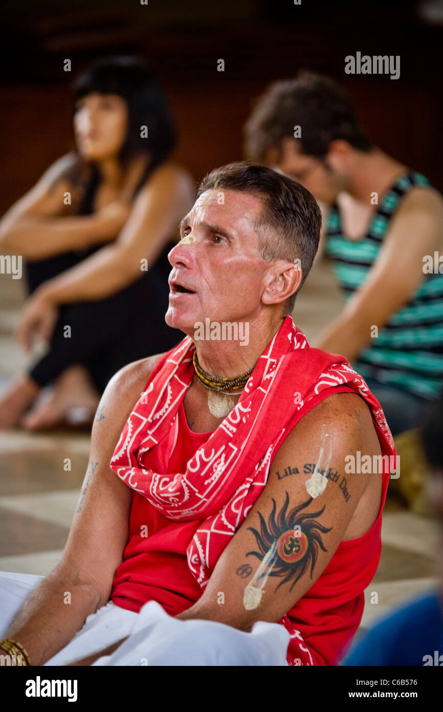 An Indian American chants while worshiping at a Hindu temple in Laguna Beach, CA. Note Chakra Wheel tattoo with Om symbol. Stock Photo