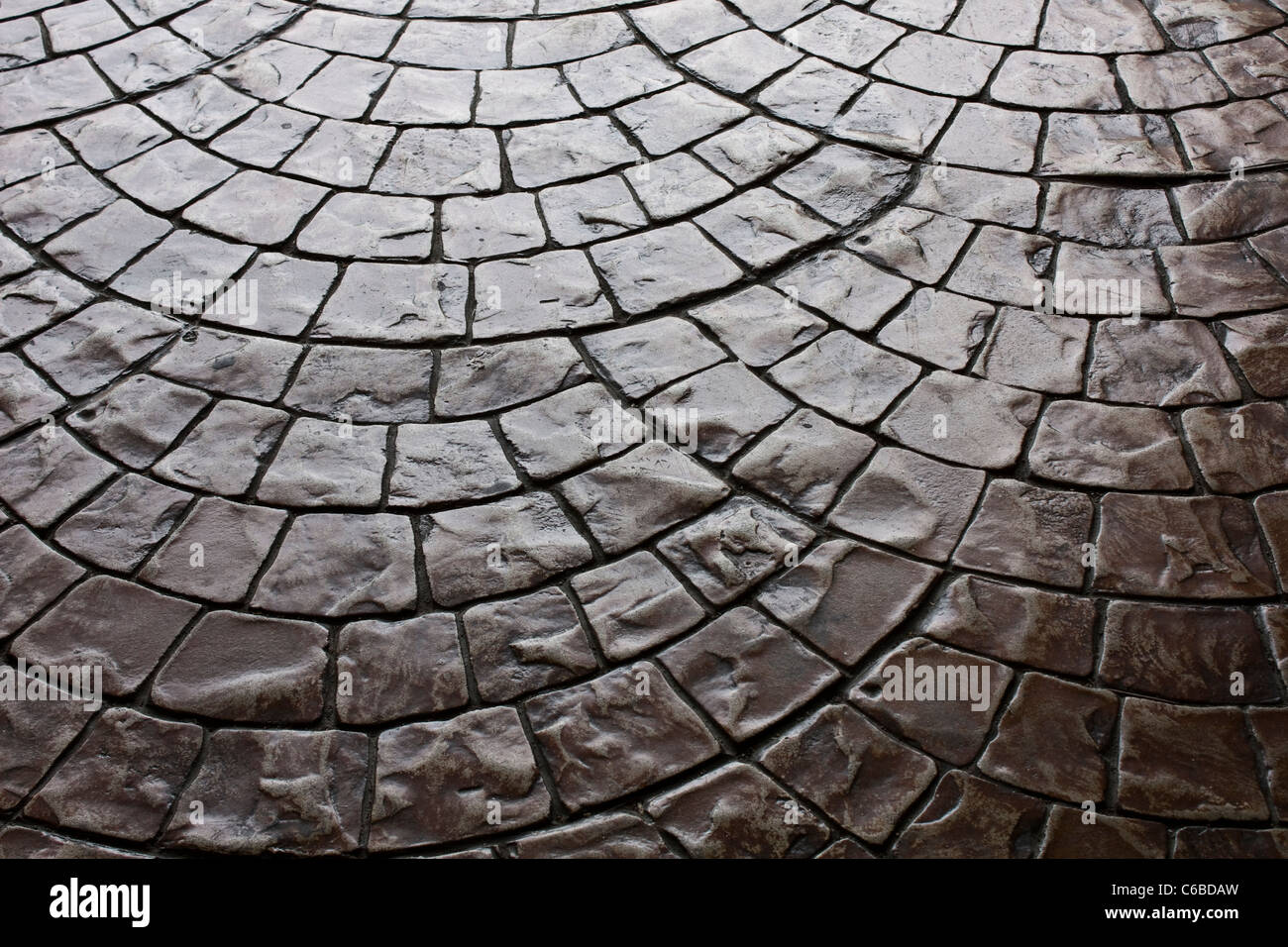 Dark rustic floor paving stones layed in a rounded pattern Stock Photo