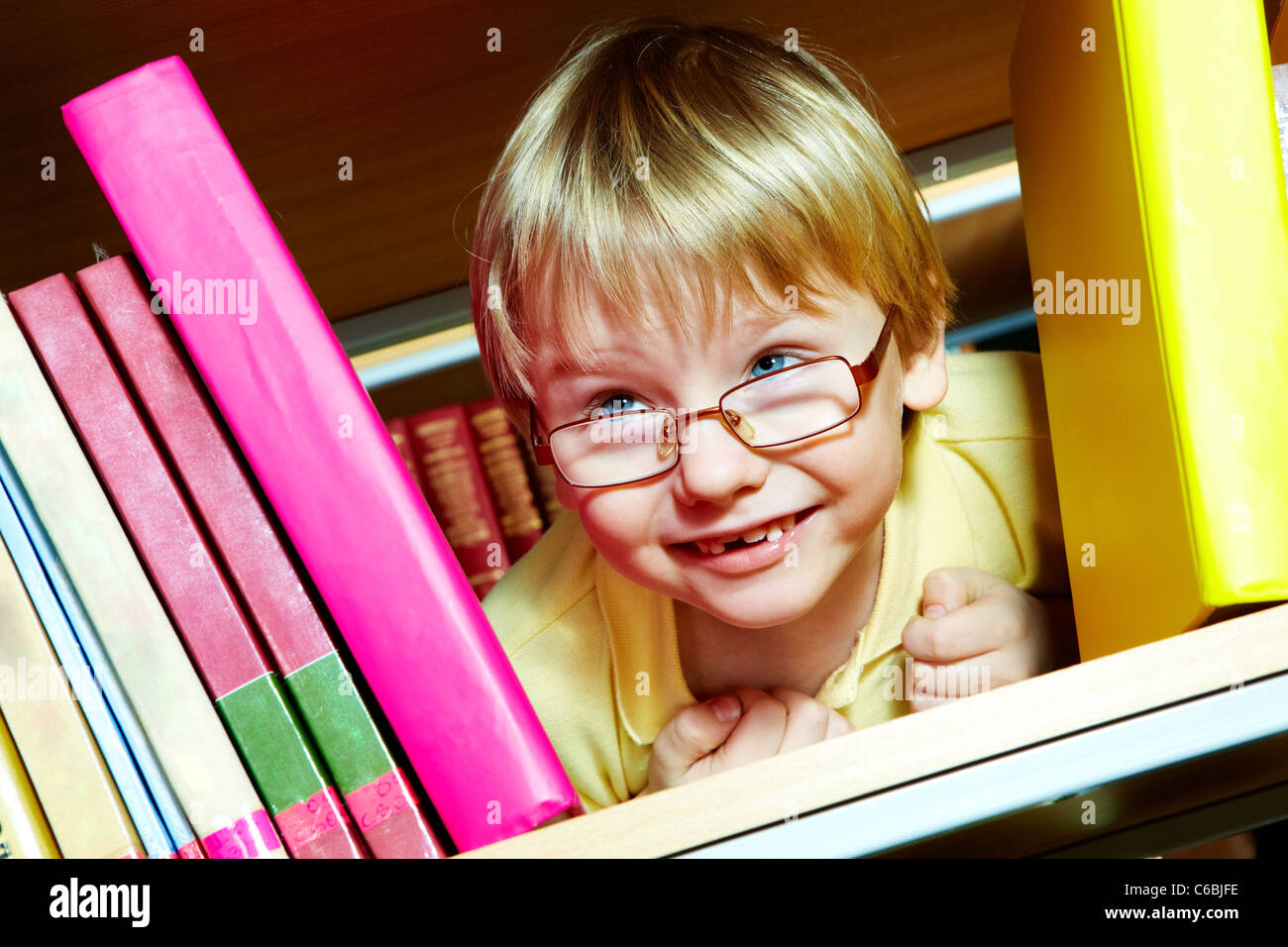 Portrait of clever boy looking from between books in library Stock