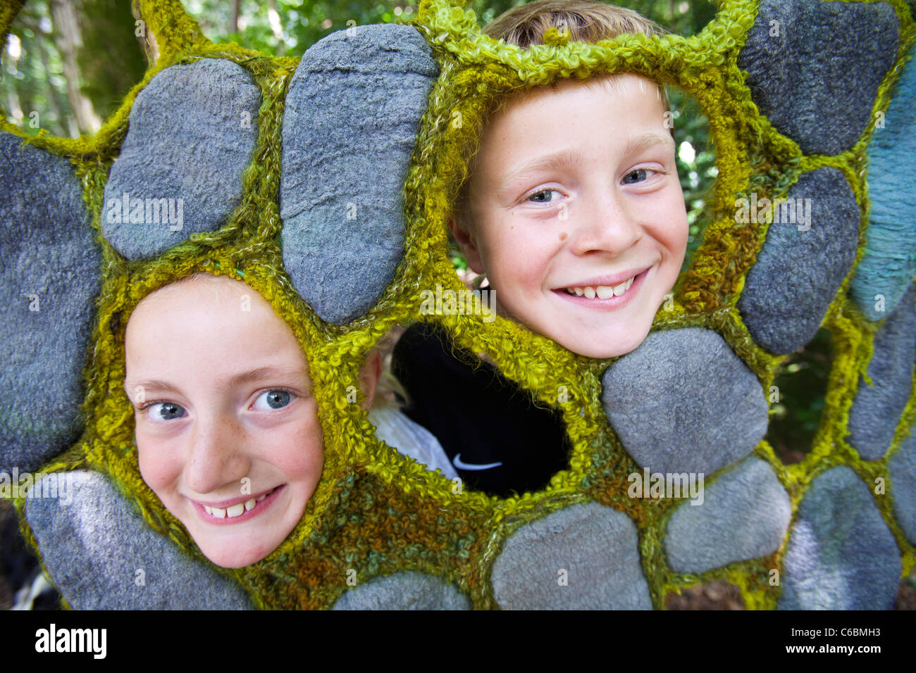 A young girl and boy poke thier faces into a hole in a textile design by Dianne Standen displayed in the grounds of Rydal Hall Stock Photo