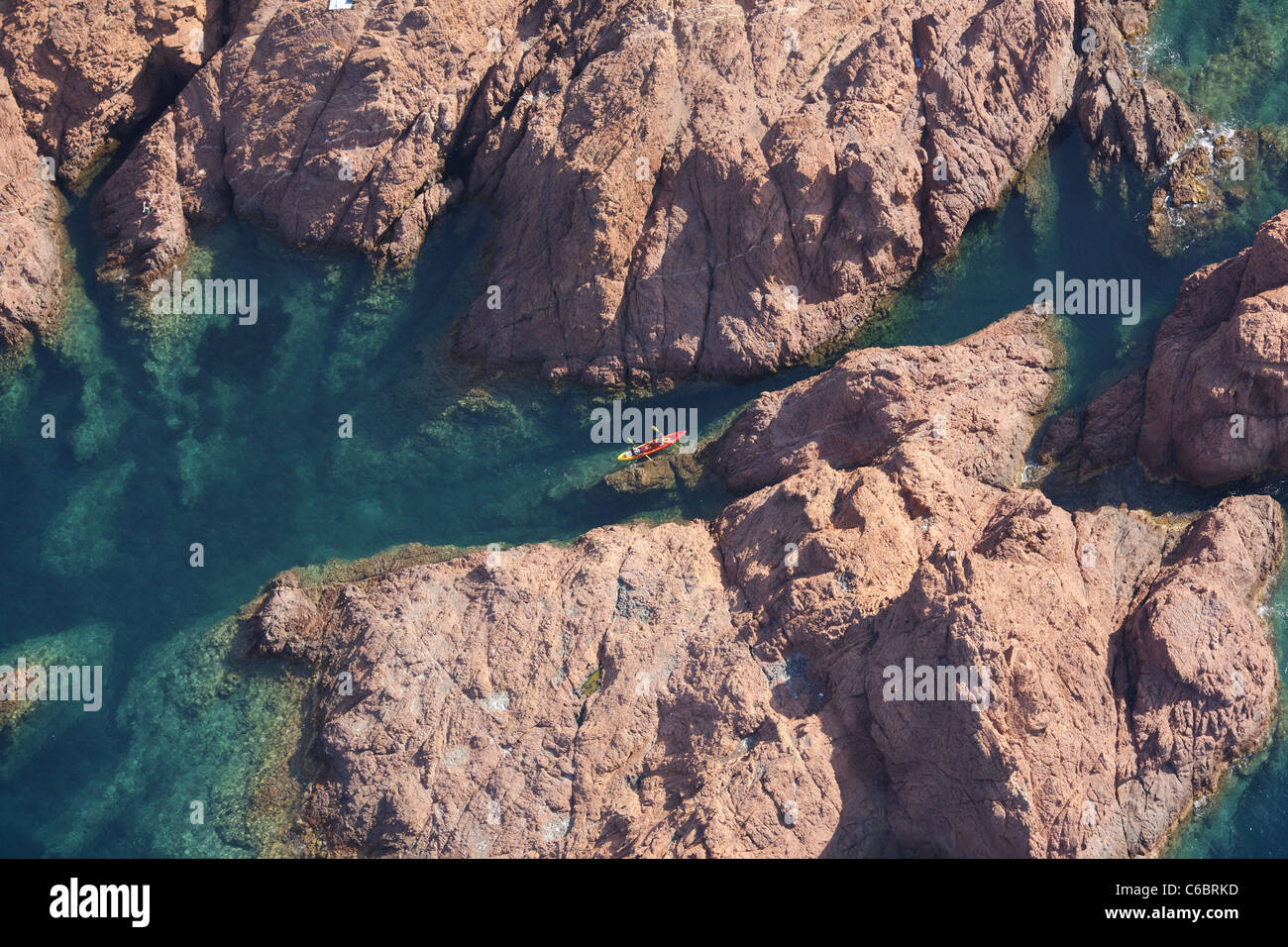 AERIAL VIEW. Couple kayaking in a narrow waterway in a landscape of red volcanic rock. Esterel Massif, Cap Dramont, Saint Raphaël. French Riviera. Stock Photo